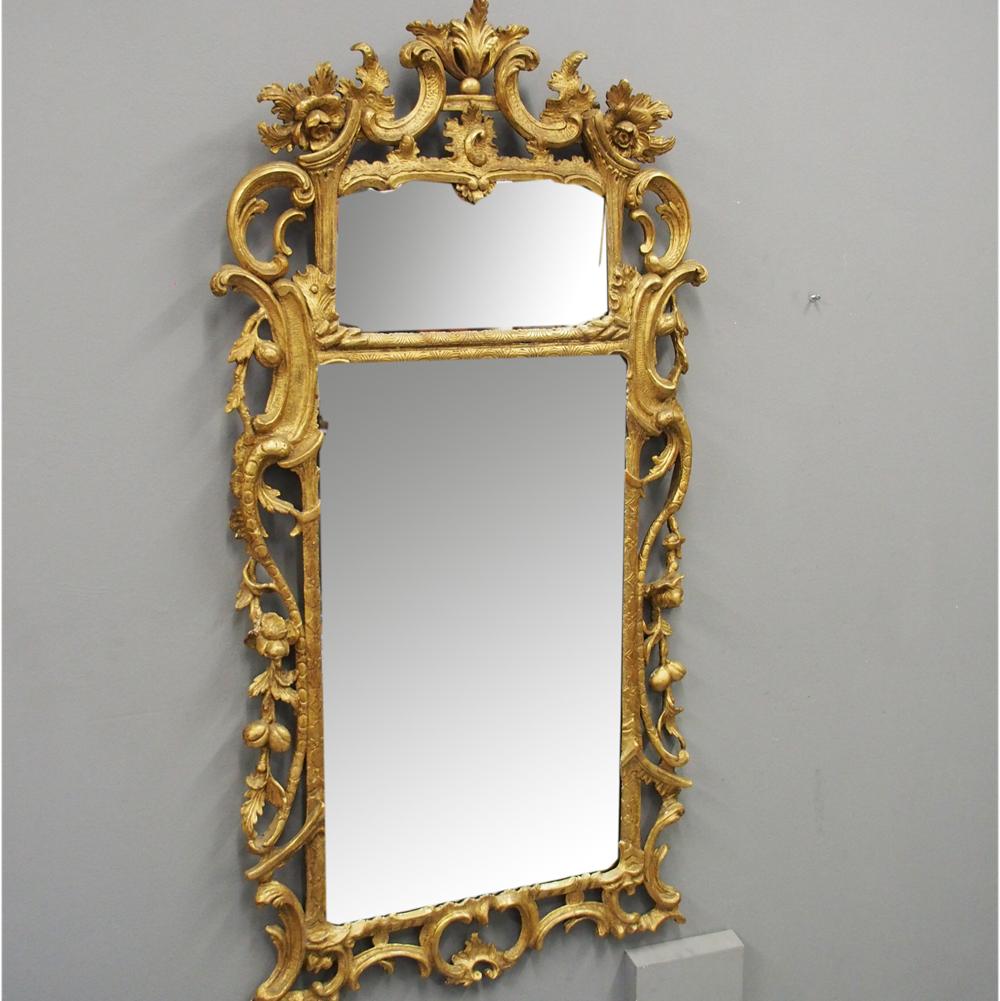 George II carved giltwood mirror in the manner of William Kent, circa 1740. The top has foliate carving, with C-scrolls and s-scrolls held in place by a combination of shaped brackets. It has a small mirror separated by a gilded double beading above