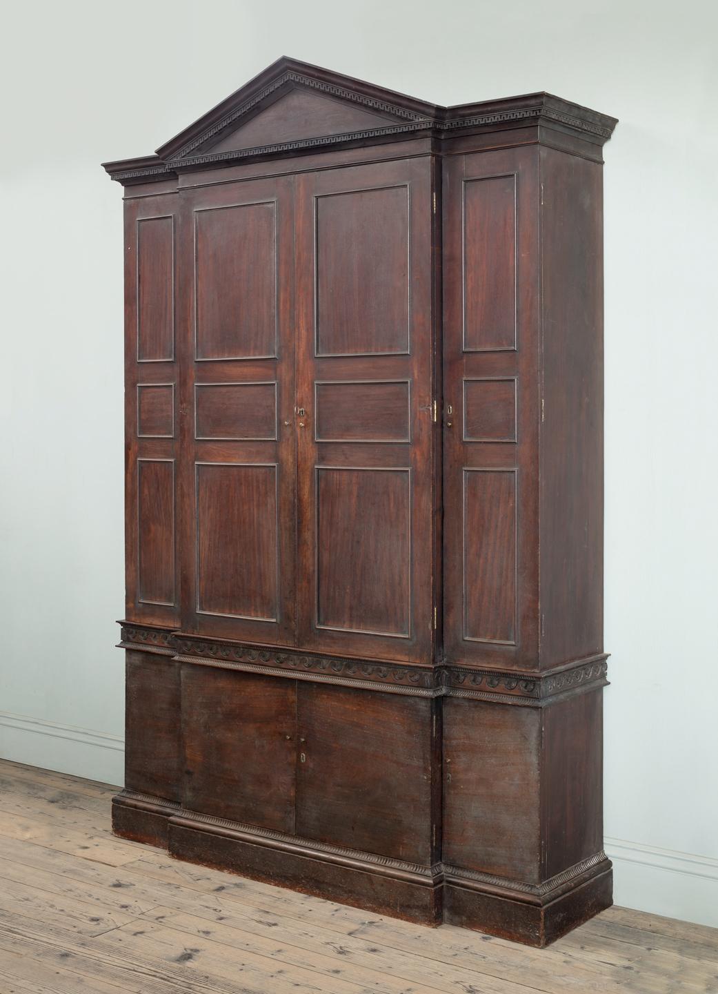 A Magnificent George II Carved Mahogany Breakfront Library Cabinet of Architectural Form

The pedimented dentil cornice above four panel doors, a waisted Vitruvian scroll fluted frieze and four further doors, on carved and moulded plinth.
English,