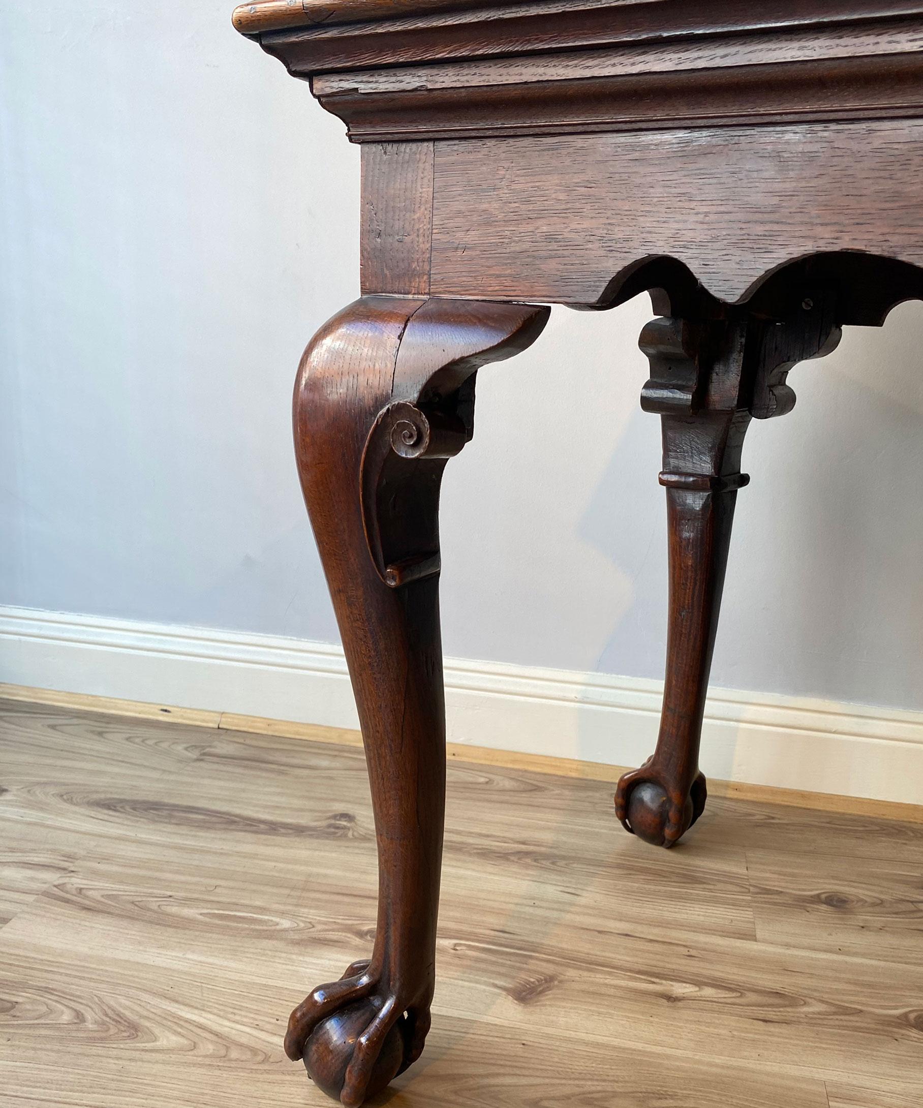 A handsome George II oak centre/ writing table; the well figured top above a shaped frieze and raised on powerful cabriole legs which have C scroll ear pieces and terminate in crisply carved claw and ball feet. The design of the table's claw and