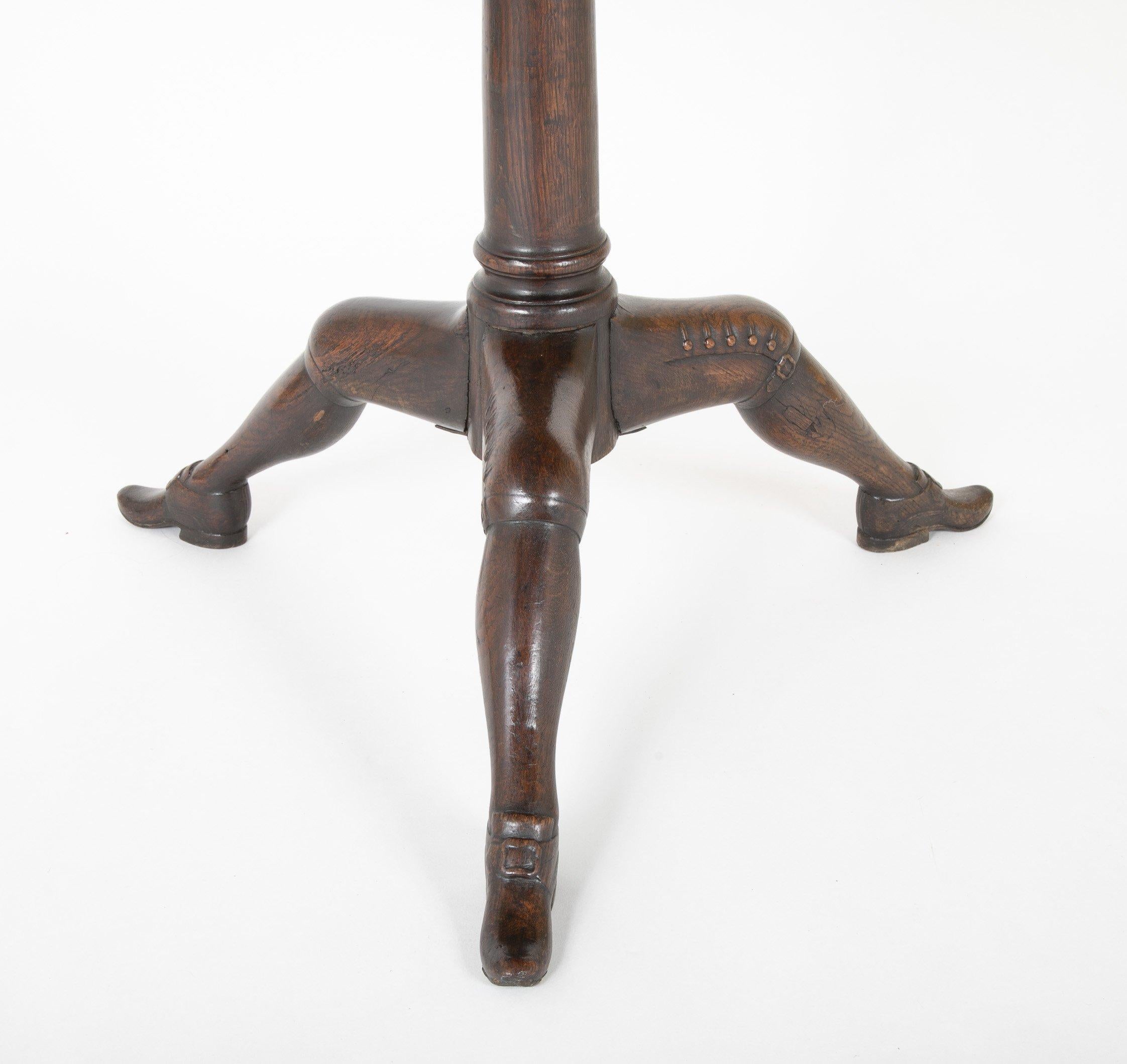 A George II oak tilt-top table with knickered legs made on the Isle of Man. English, circa 1750. Attributed to this small isle by the distinctive carved leg decoration terminating in boots, similar to the island's flag. The additional carved straps