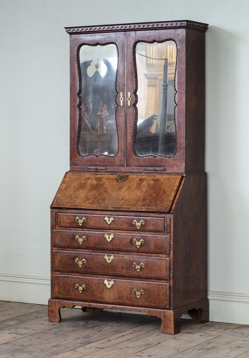 A Superb George II Carved Walnut and Feather Banded Bureau Bookcase, attributed to Giles Grendey.

The scroll cornice above a pair of shaped mirror doors enclosing shelves and pigeon holes, the bass with a rectangular fall enclosing a fitted