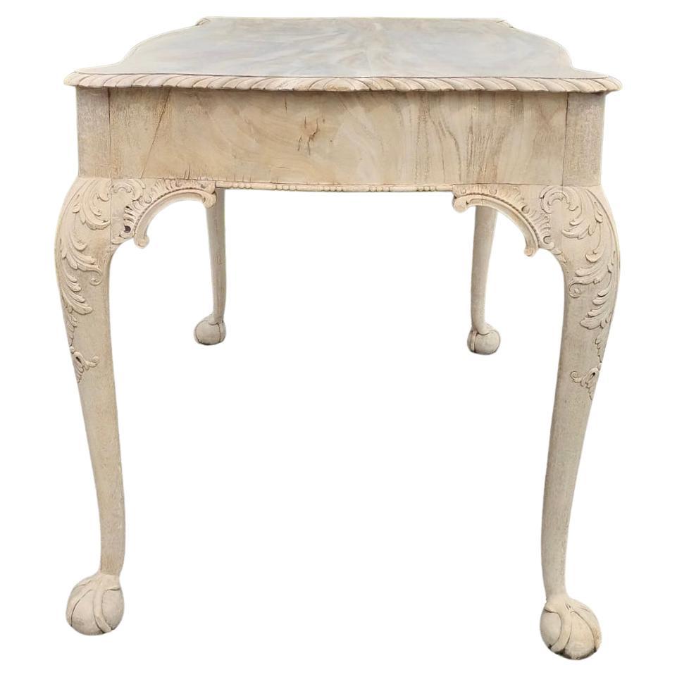 Bibliothèque de style George II en acajou blanchi - Table centrale. Le bois d'acajou sculpté en finition blanchie contribue à l'aspect luxueux de la table. La table est de forme rectangulaire. Les pieds cabriole sont sculptés de volutes complexes