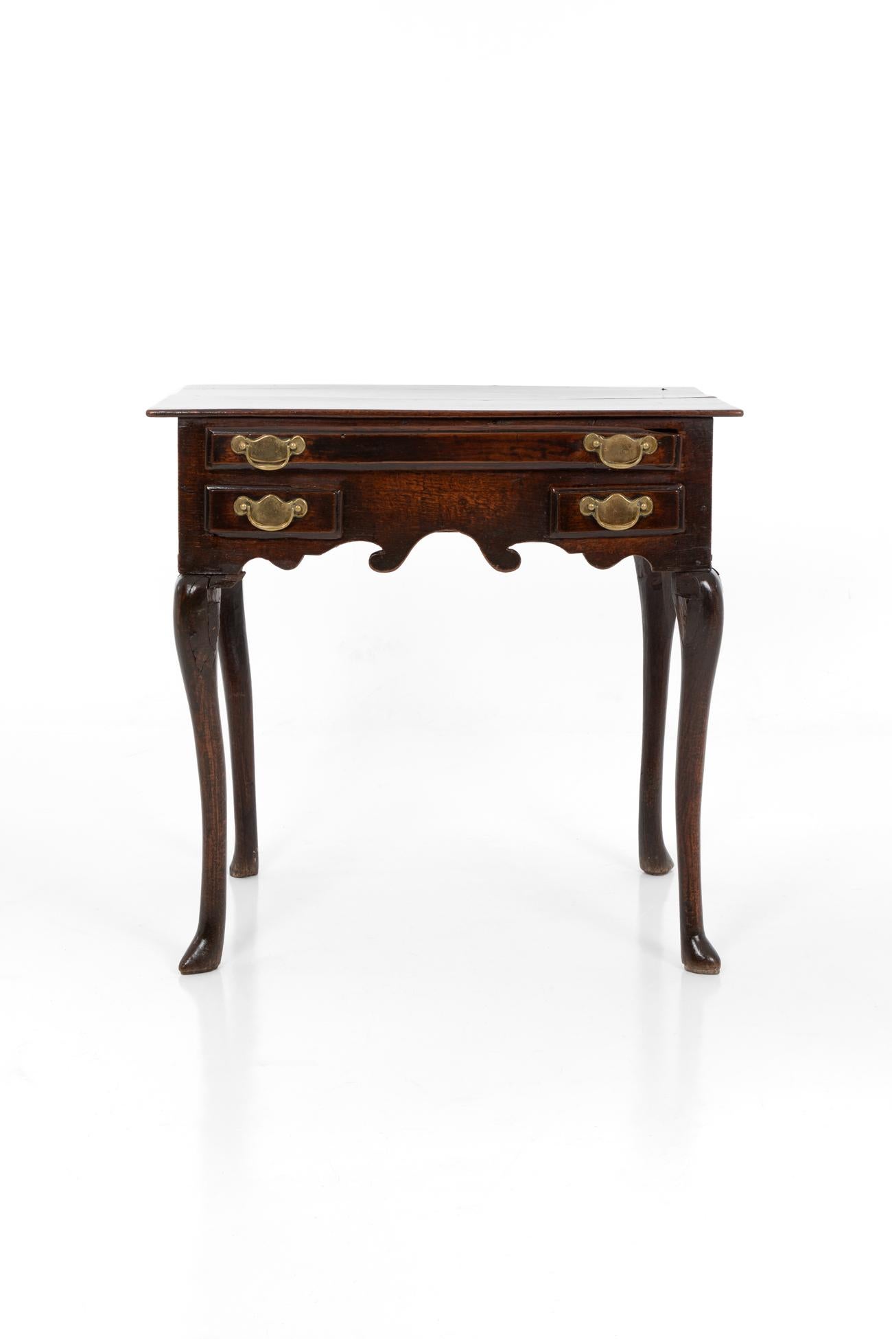 A George II country oak lowboy with a moulded rectangular two plank top. Single frieze drawer over two short drawers, with brass drop handles on pierced back plates. Shaped apron on slender cabriole legs on trifid feet.
English, circa