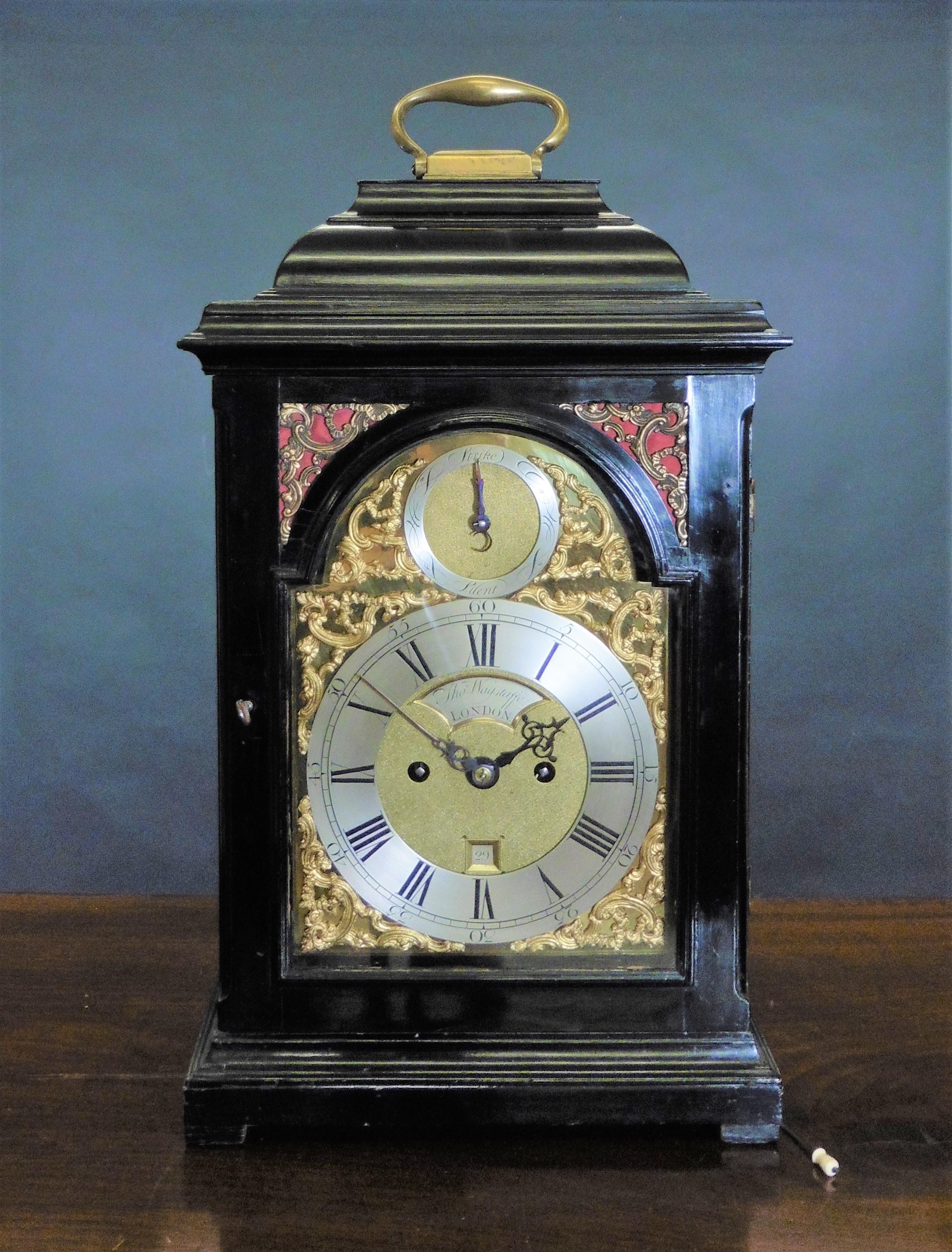 George II bracket clock by Thomas Wagstaffe, London

Ebonised bell top case surmounted by a hinged brass carrying handle standing on a raised plinth and resting on four pad feet. Cast brass upper quadrant silk lined frets, glazed side windows and