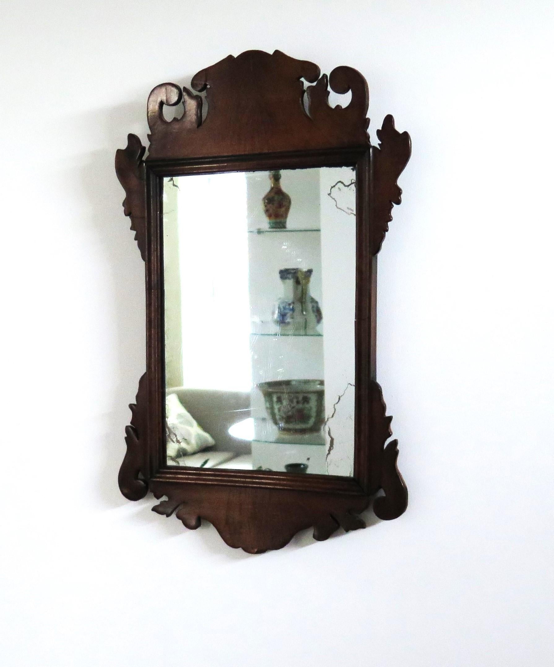 This English hanging wall mirror is from the mid 18th Century, George 11nd period circa 1750.

It has a softwood frame construction, probably pine with hardwood figured walnut veneers to the front, which are all fret-cut, with cresting and base