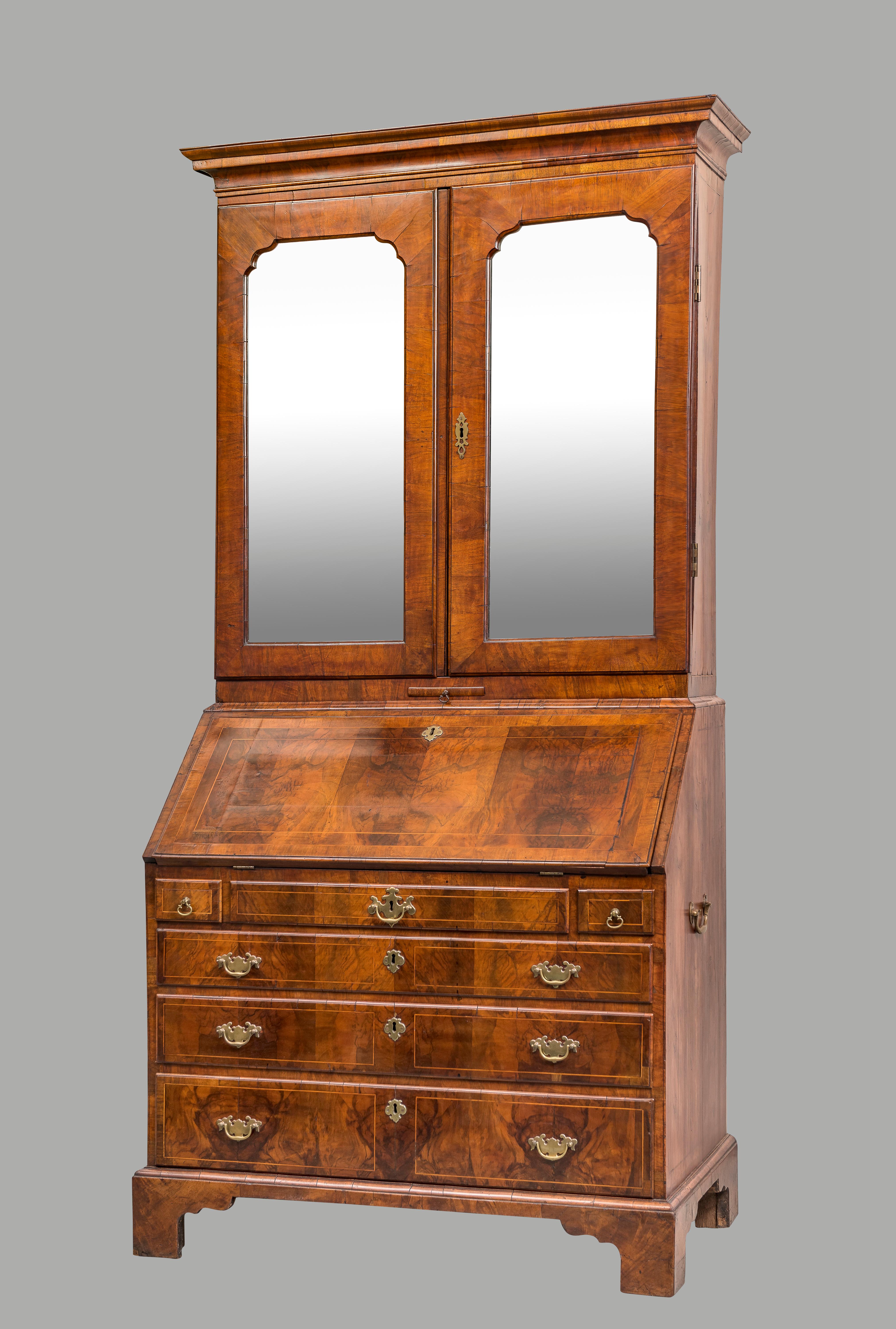An English George II inlaid walnut secretary cabinet with mirrored doors, the upper stage with 2 interior adjustable shelves over 4 small drawers above a single candle slide, the lower with a fall front bureau containing a well-fitted interior with