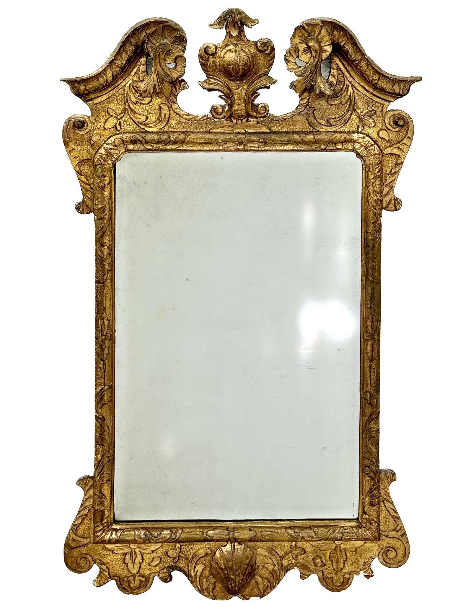 18th century George II giltwood mirror featuring beveled edges and mounted in a gilt frame. Allover carved with scrolling acanthus leaves on a mottled or sanded ground. Geometric-carved border, surmounted by an acanthus-carved broken arch pediment