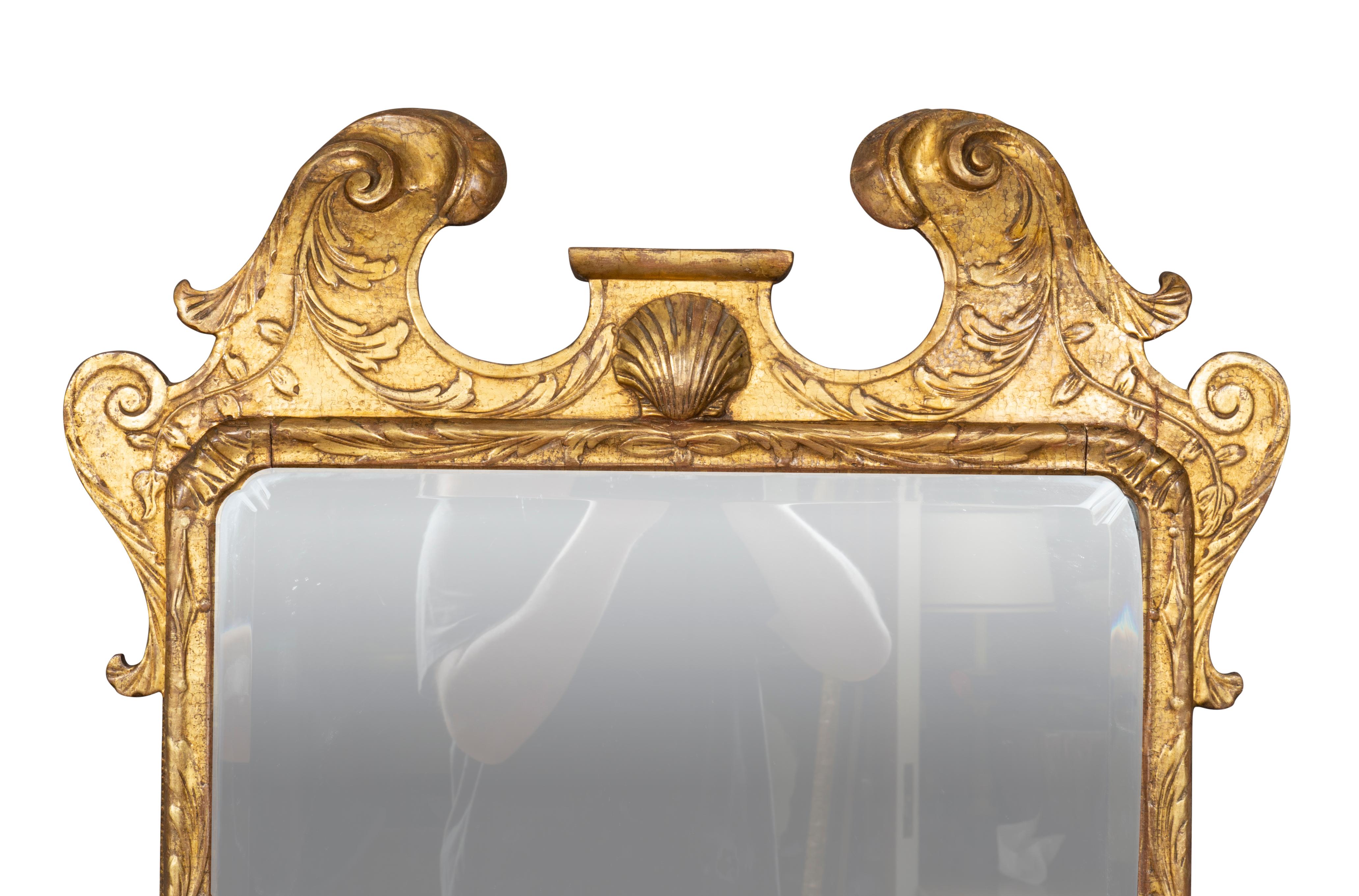 With original gilding. Broken arch pediment with central shell carving over a beveled mirror plate set within a frame with carved shaped corners , backplates that once held candle arms.