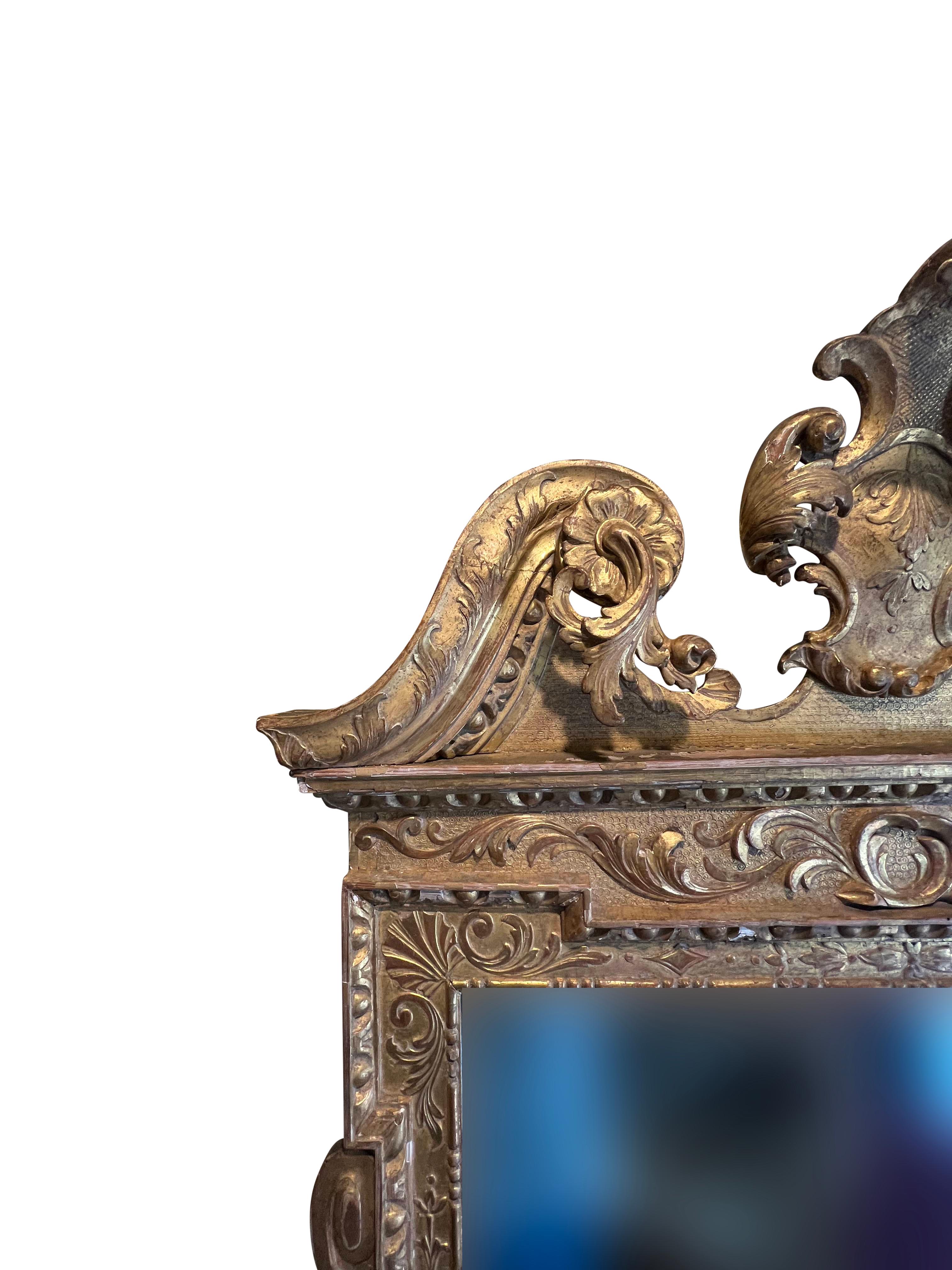 With central carved cartouche within a scrolled arched pediment over a mirror plate set in an egg and dart and bead and reel frame. The base of the frame with brass plates that once held candle arms.