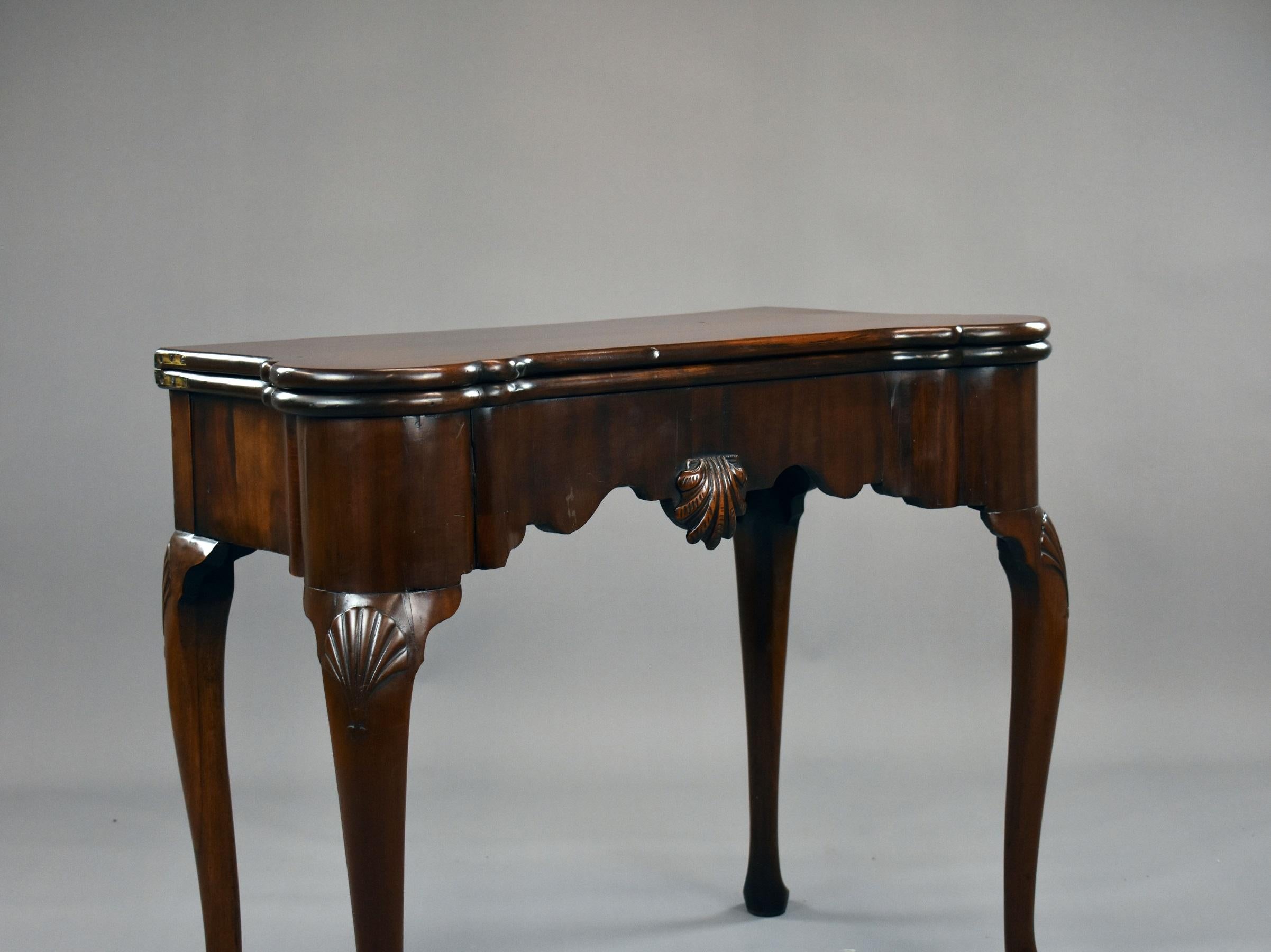 George II Irish Mahogany card table with carved scalloped shell on frieze, raised on shell carved cabriole legs on pad feet. The table opens to reveal a green baize lined playing surface inset with counter wells.