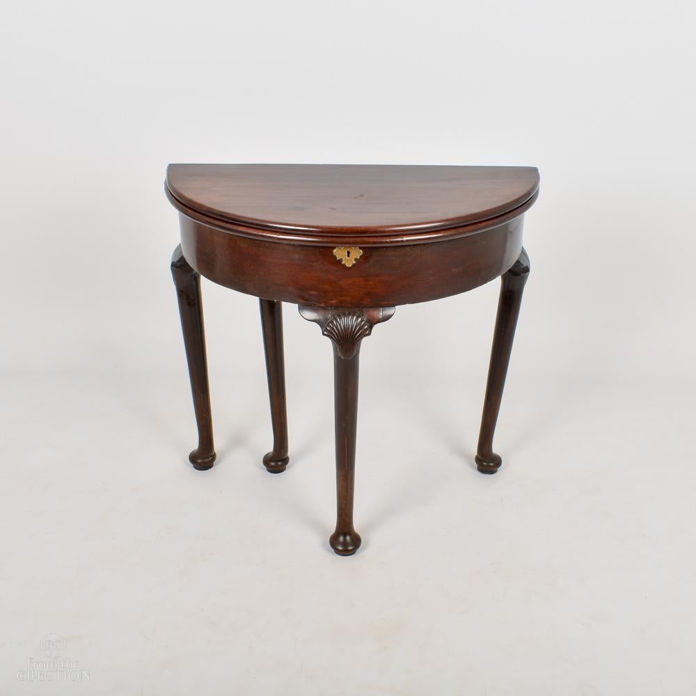 A fine quality Georgian Irish mahogany demi-lune tea table, folds out to a circular table with shell detail at the top of the front leg. On four legs with pad feet. Of excellent rich color.
