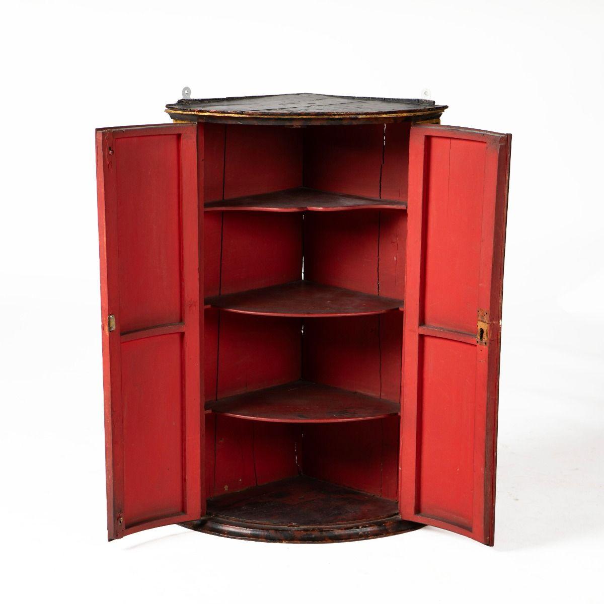 English hanging corner cabinet with a bowed front from the George II period, circa 1730.
Originally decorated with japanned motifs executed in gold leaf on a black and red ground, depicting birds, houses, trees, and figures.
Fitted with original