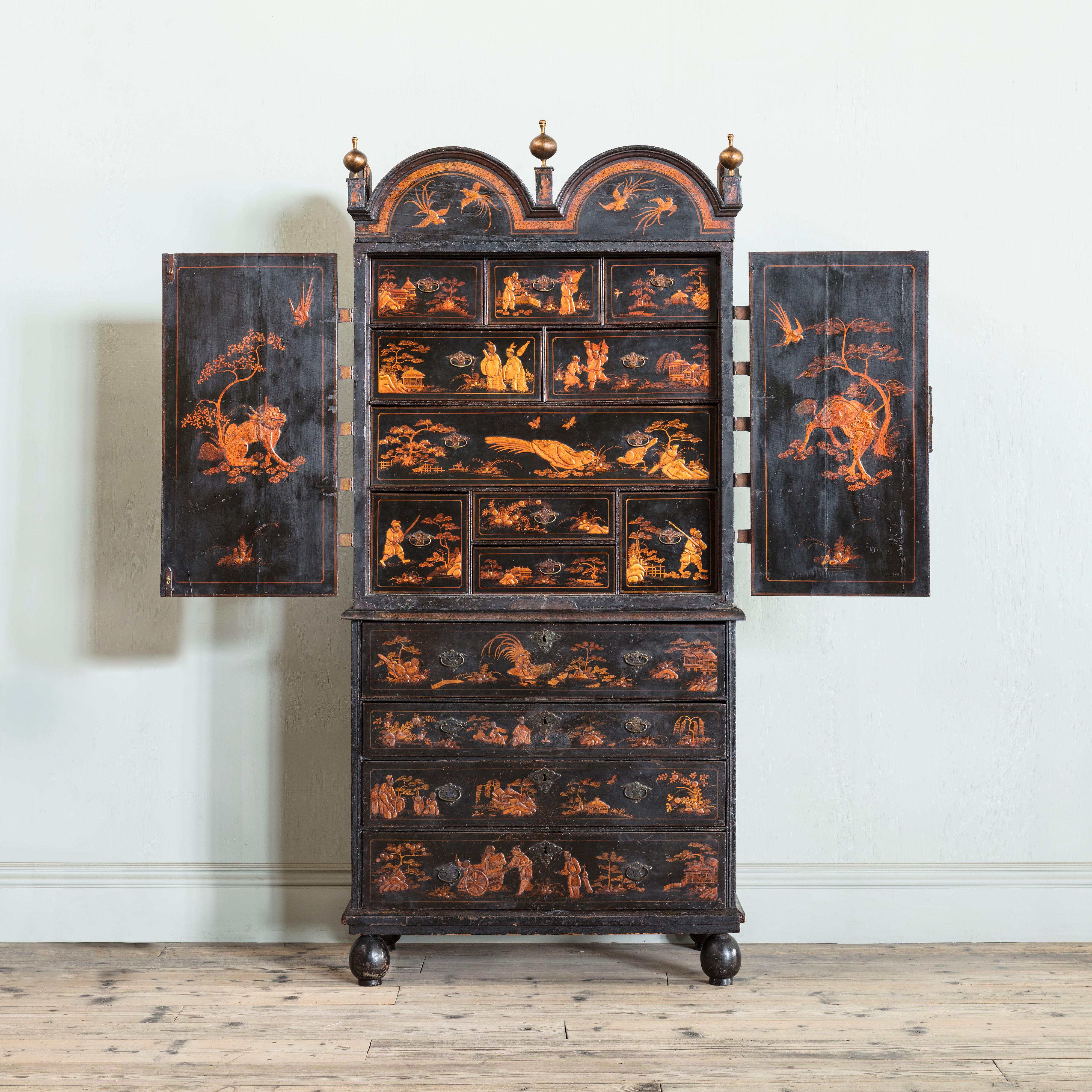 A George II Lacquer Cabinet on Chest with double dome cornice and three ball finials, above two cabinet doors with robust banded hinges, opening to reveal an interior of ten drawers, above a secretaire chest of four graduated drawers, on bun