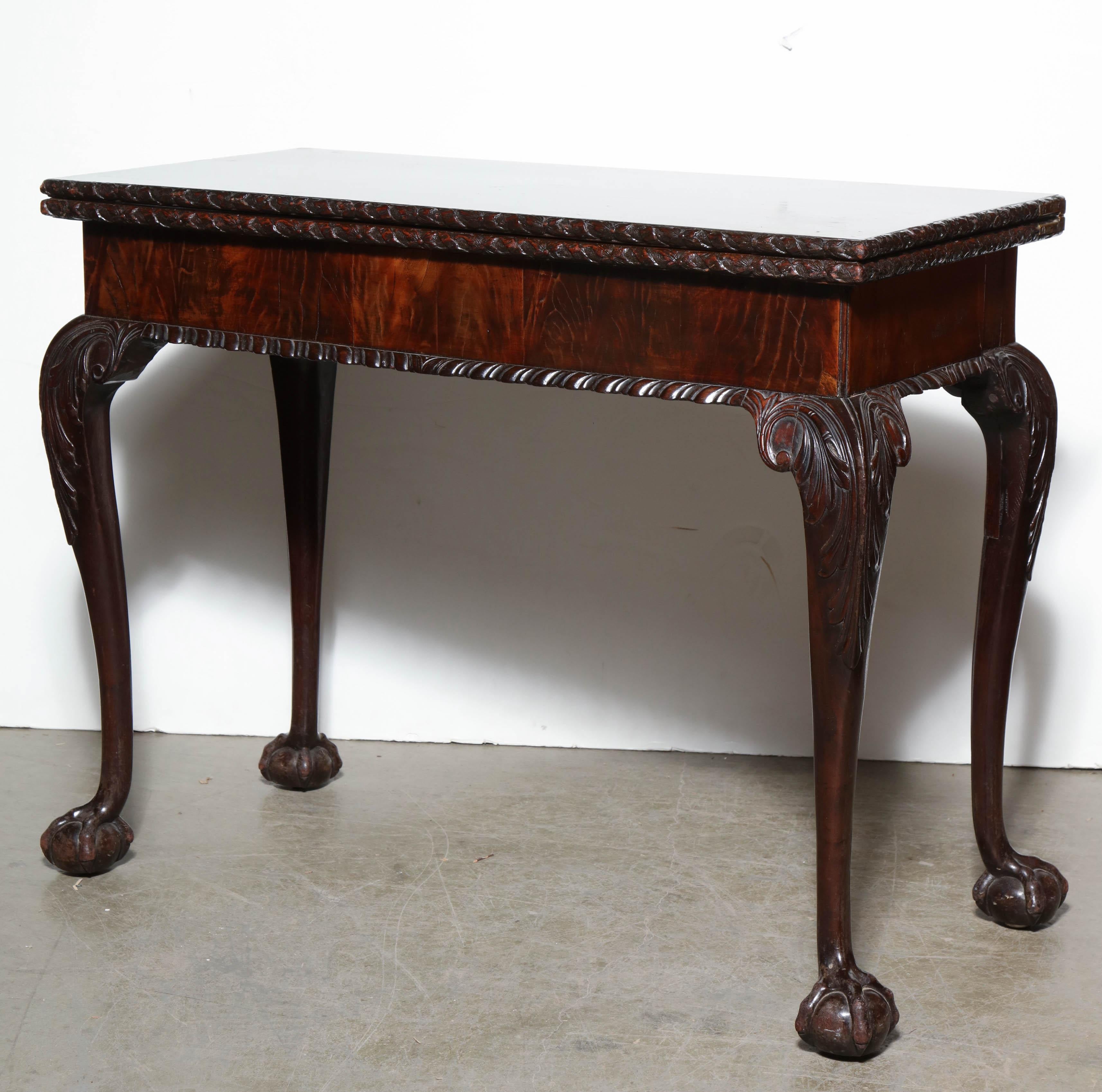 George II mahogany concertina action ball and claw foot game table with gadrooned apron, ribbon and blossom carved edges and gold tooled leather interior.