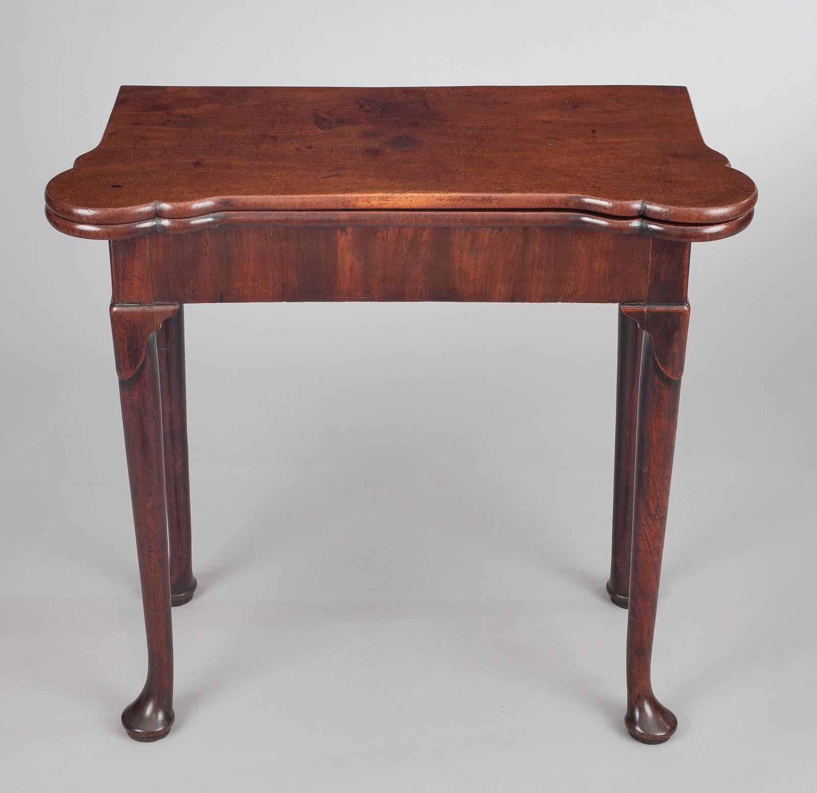 George II period mahogany fold-over card table, the rectangular top with projecting shaped rounded corners, raised on four legs with distinctive carved lappet detail to the top of the leg and pad feet. It opens with a concertina action, making a