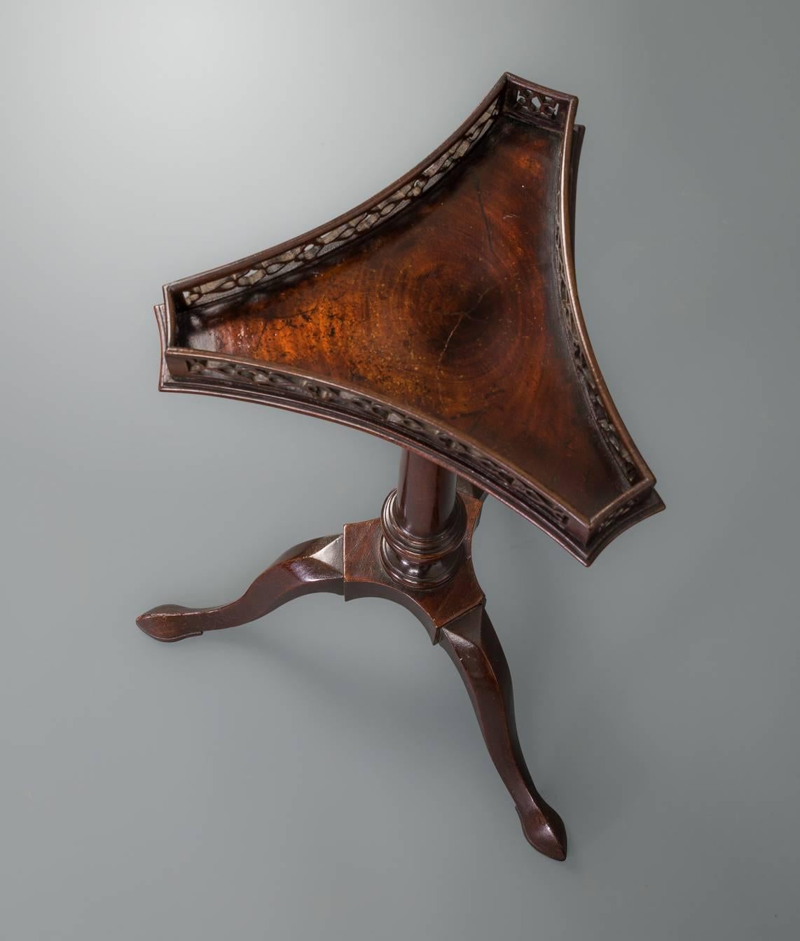 The triangular figured top with in curved sides with a conforming pierced fret gallery on an iron topped and ring turned column supported on a triangular solid platform with conforming in curved sides, the legs of chamfered cabriole form terminating