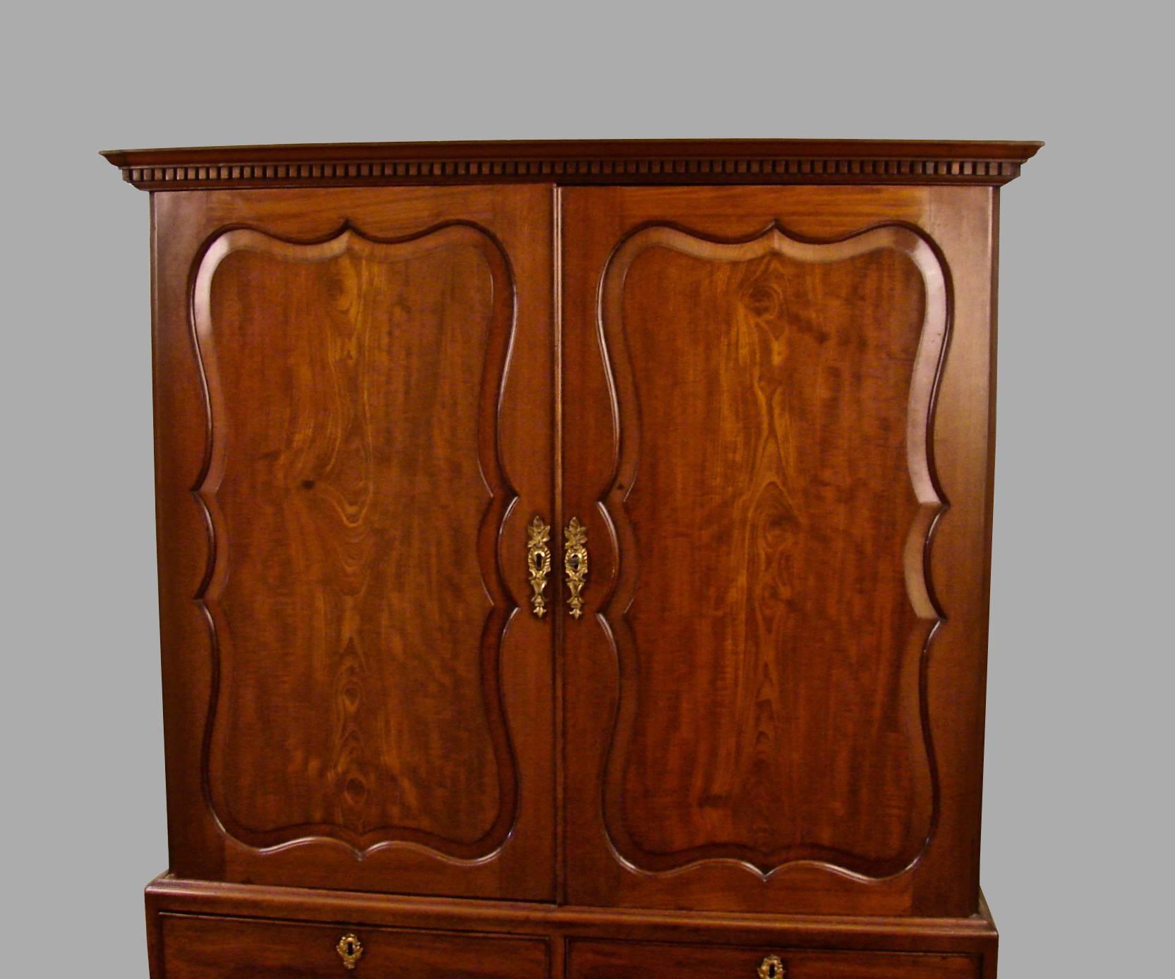 A George II period mahogany 2 section linen press in the manner of Giles Grendy, the upper stage with cartouche panelled doors enclosing a single shelf, the lower section with 2 short and one long drawer with gilt brass hardware resting on bracket