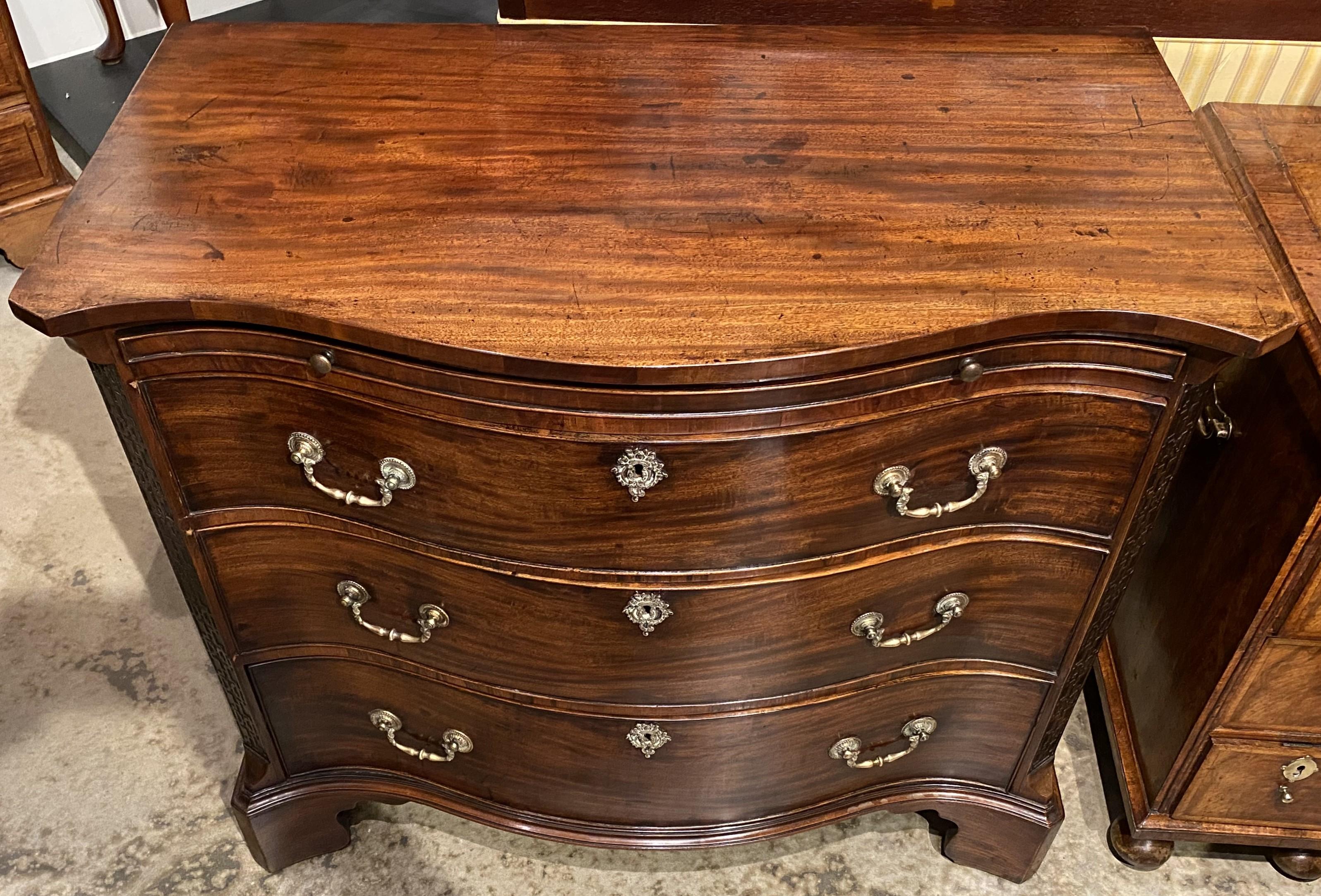 Bella cassettiera a serpentina in mogano inglese di Giorgio II con piano in pelle che scorre su tre lunghi cassetti, ciascuno con pesanti tiretti in ottone e scanalature decorative, affiancati da angoli a sbalzo intagliati, tutti sostenuti da