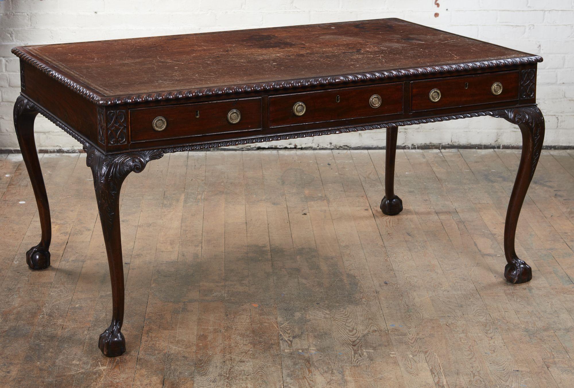 Very fine George II mahogany writing table, the leather-lined top with gilt tooling and banded edge, the edge with rich gadroon carving, over three drawers, standing on boldly carved cabriole legs with acanthus leaf knees and ball and claw feet, the