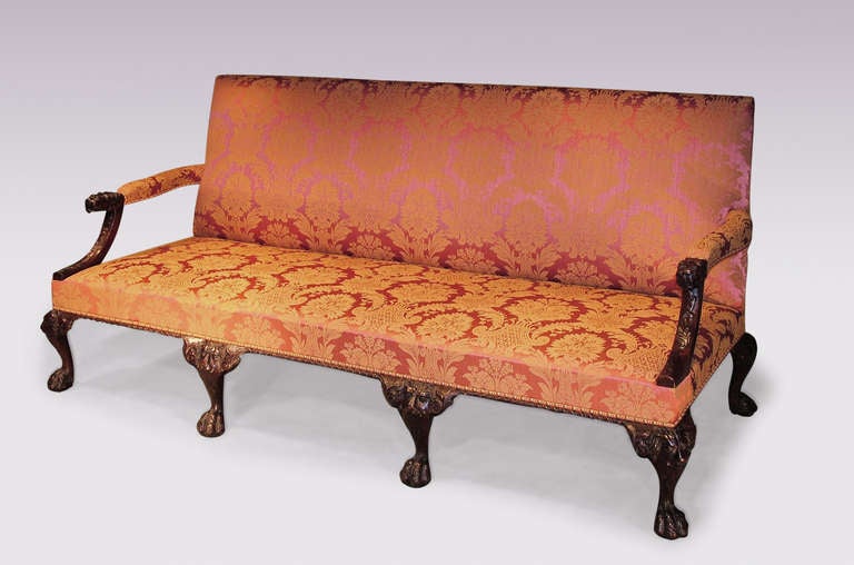 An impressive George II revival mahogany settee upholstered in red silk damask, having padded arms with lion’s head terminals raised on curved leaf carved supports. The settee with gadrooned edging to the frieze, supported on lion-mask cabriole legs