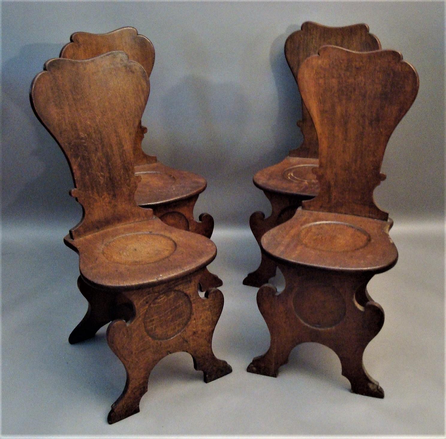 George II set of four oak scabello hall chairs, of the traditional silhouette scabello form; the slightly curved, vase shaped back above the shaped seat with the typical circular dish, raised on shaped supports united by a curved