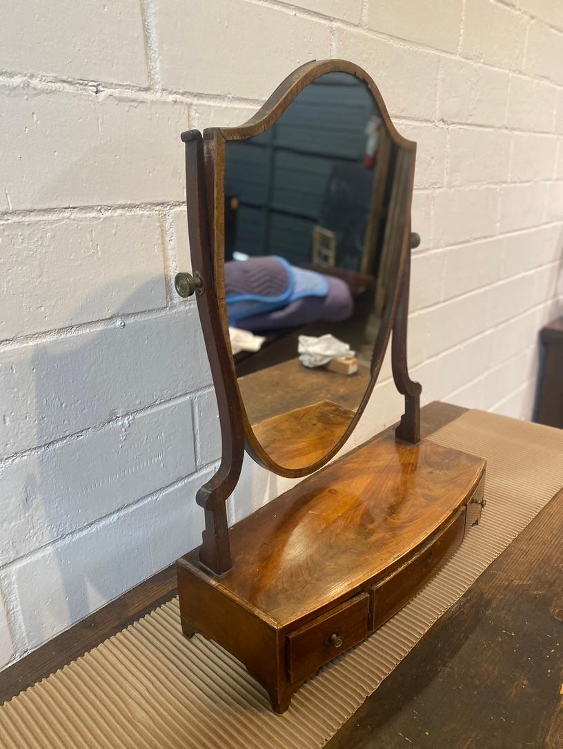 Antique Georgian shield framed dresser/shaving mirror with original antique glass. All dovetail construction , and finished in crotch mahogany with boxwood stringing bordering the three drawers. All original brass hardware, natural patina, and the