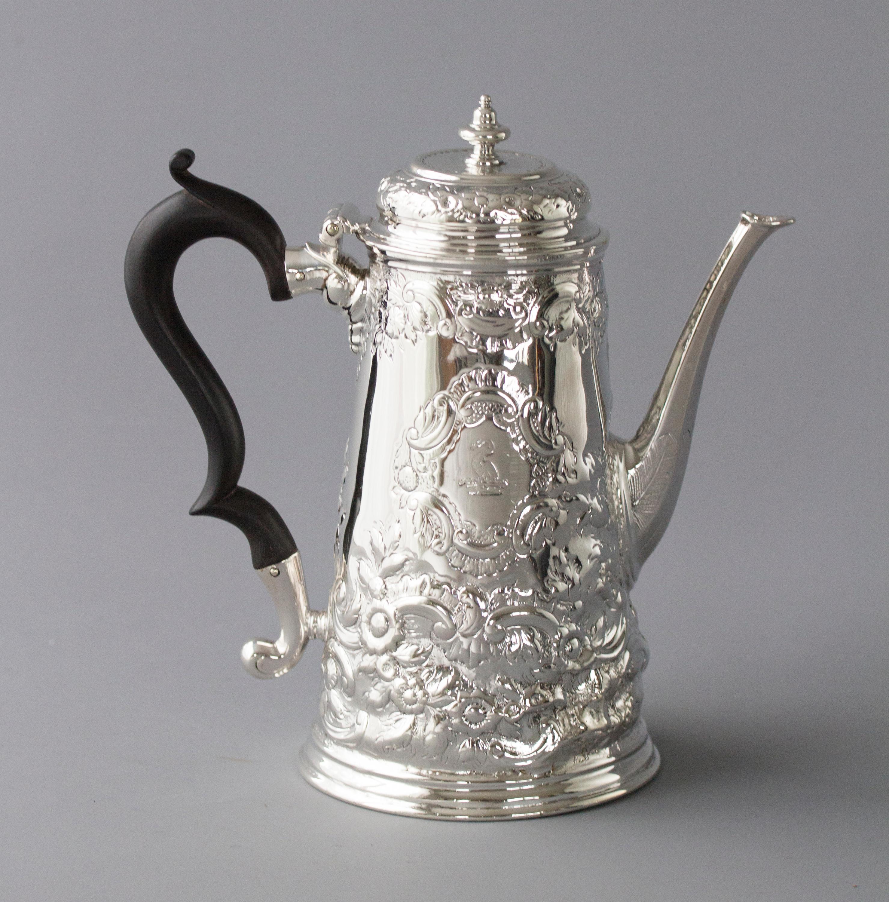 A fine George II silver coffee pot of tapering form embossed all over with floral and foliate motifs, each side with a cartouche, one with the crest of a bird emerging from a coronet and the other with a monogram. The octagonal faceted spout with