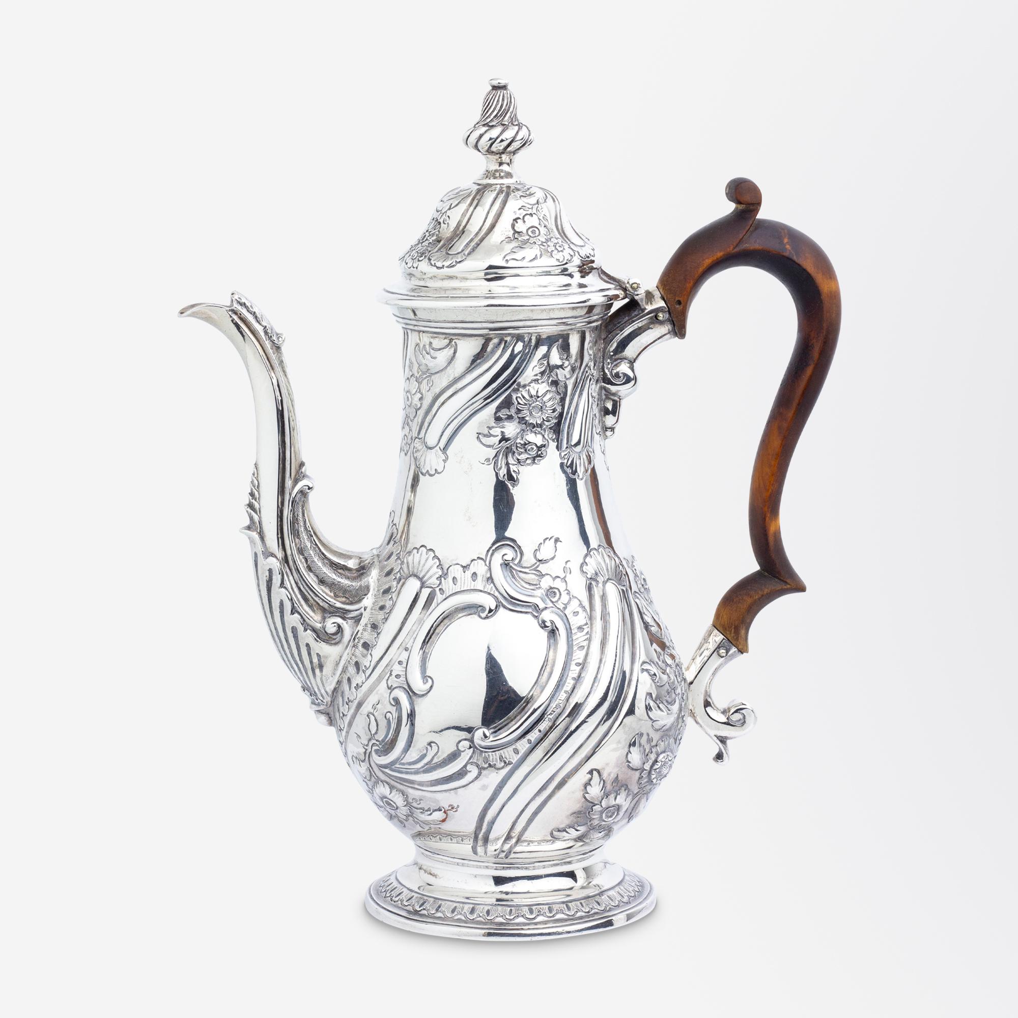 A fine George II sterling silver coffee pot with a wooden handle, floral repousse details and a crest with rubbed maker's mark likely for William Skeen. The coffee pot is very much in the Rococo taste of the early to mid 18th Century with