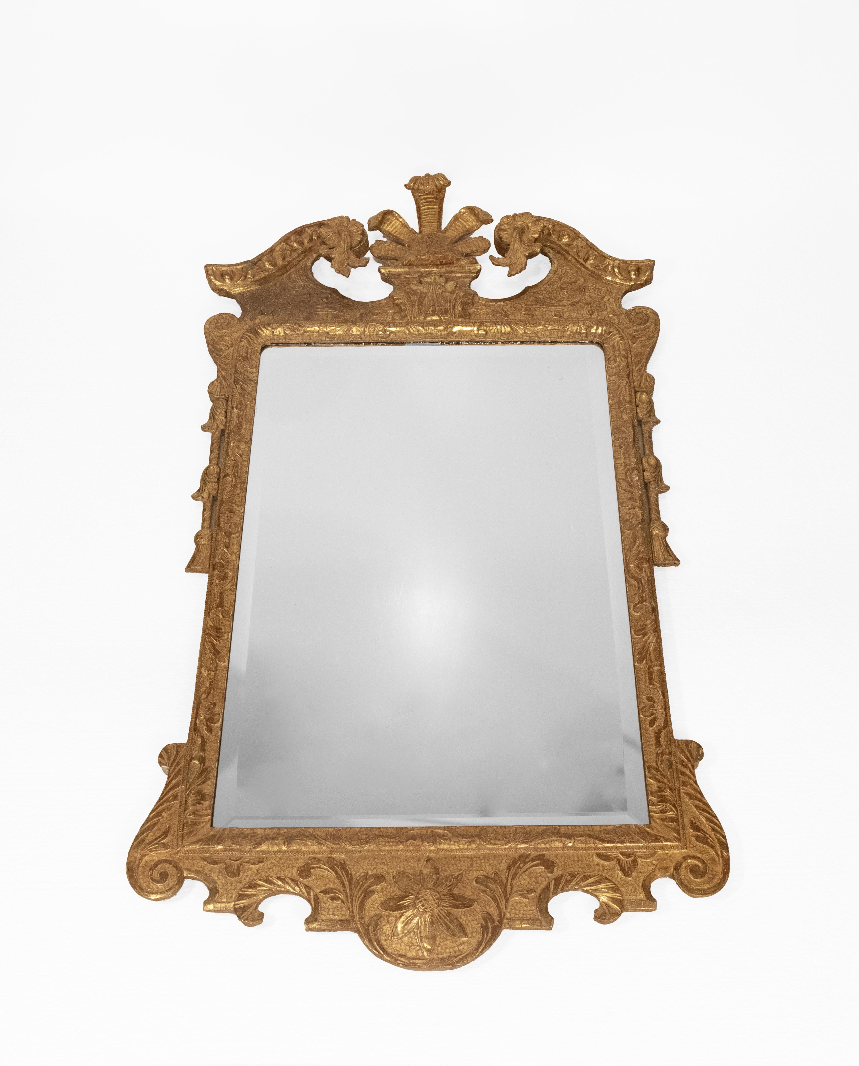 Ce miroir en bois doré de style George II du XVIIIe siècle présente un cadre sculpté avec des motifs de feuillage et une riche finition dorée. Le cimier est orné d'un fleuron en forme de feuille, flanqué d'une paire de détails à volutes