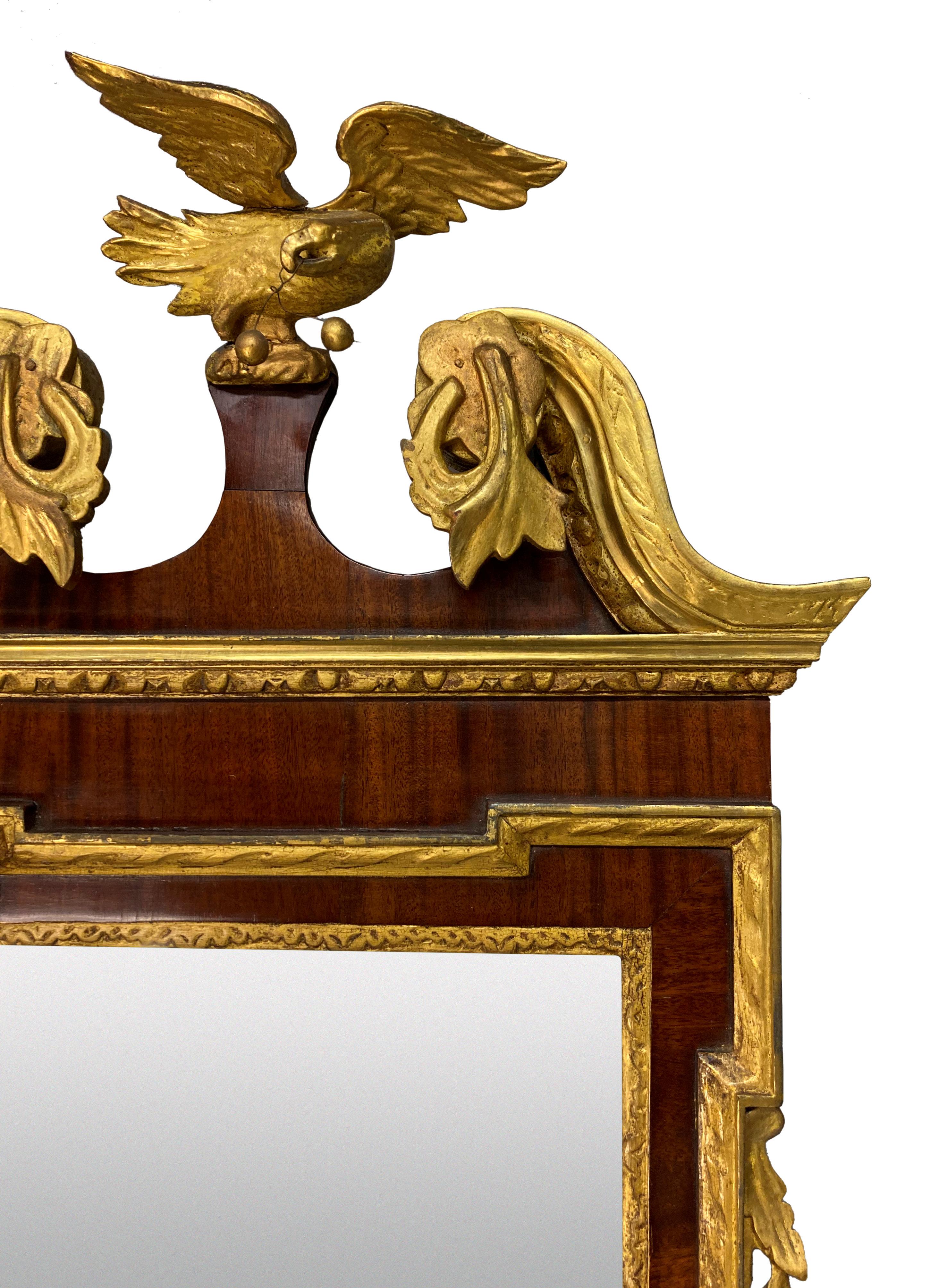 An English George II style finely carved mahogany and parcel gilt mirror. Water gilded with an architectural pediment surmounted with an eagle and with swags and foliage. The mirror plate is bevelled.