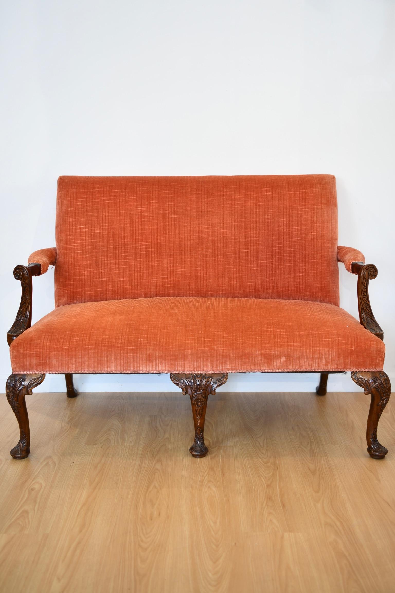 Intricately carved mahogany settee in the style of George II with open arms above detail carved pad feet and blood orange upholstery. Dimensions: 38
