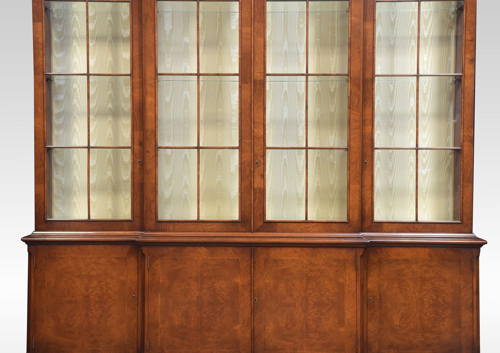 Walnut four-door display bookcase, the projecting cornice above, four large glazed doors opening to reveal the upholstered and adjustable glass shelved interior. To the base section fitted with four walnut paneled cupboard doors all raised up on