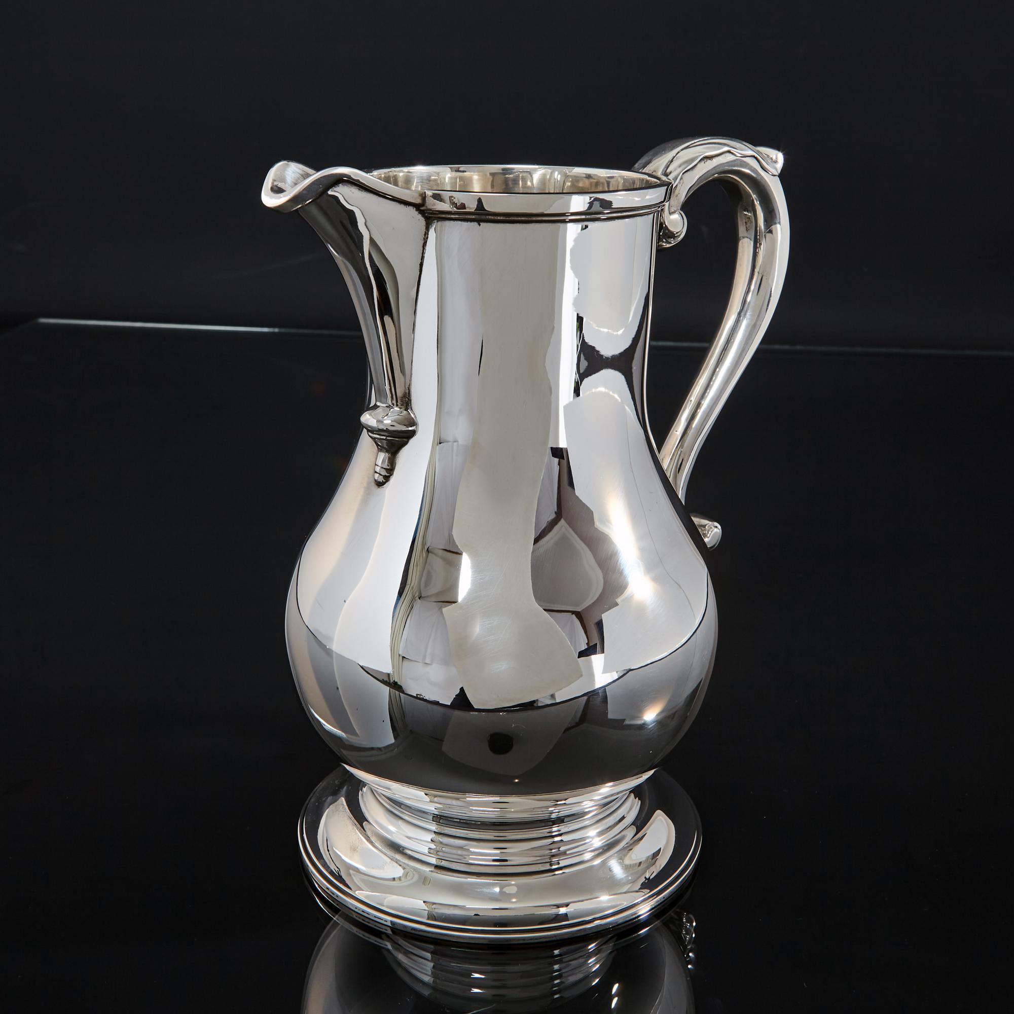 An excellent quality silver water pitcher made in the style of a classic Georgian beer jug. This silver water jug's bellied form on a spreading circular base, and featuring a scroll handle with leaf thumbpiece, are all design elements that personify