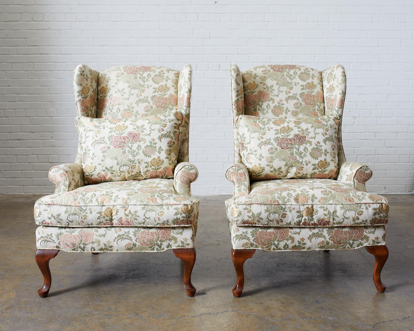 Pair of elegant wingback chairs made in the George II style. Featuring a lovely brocade upholstery of foliate and chrysanthemum patterns over a cream background. Supported by carved cabriole legs in the front and splayed legs in the rear. Large high