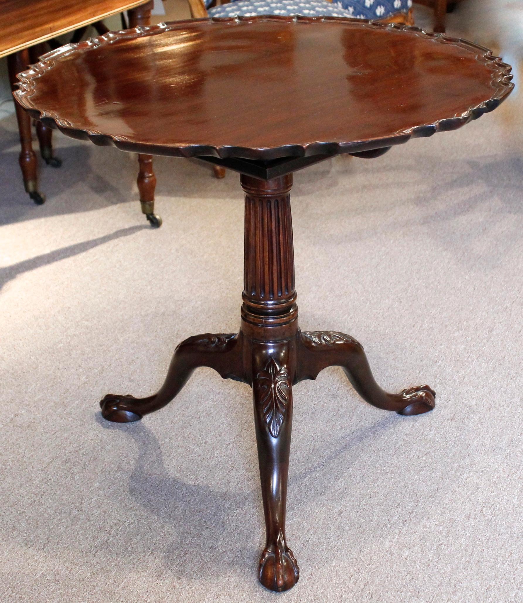 A fine ca. 1760 English single board mahogany tilt top tea table, the pedestal base carved as a substantial and handsome fluted column resting on finely carved downswept legs with carved knees and terminating in elongated ball and claw feet.