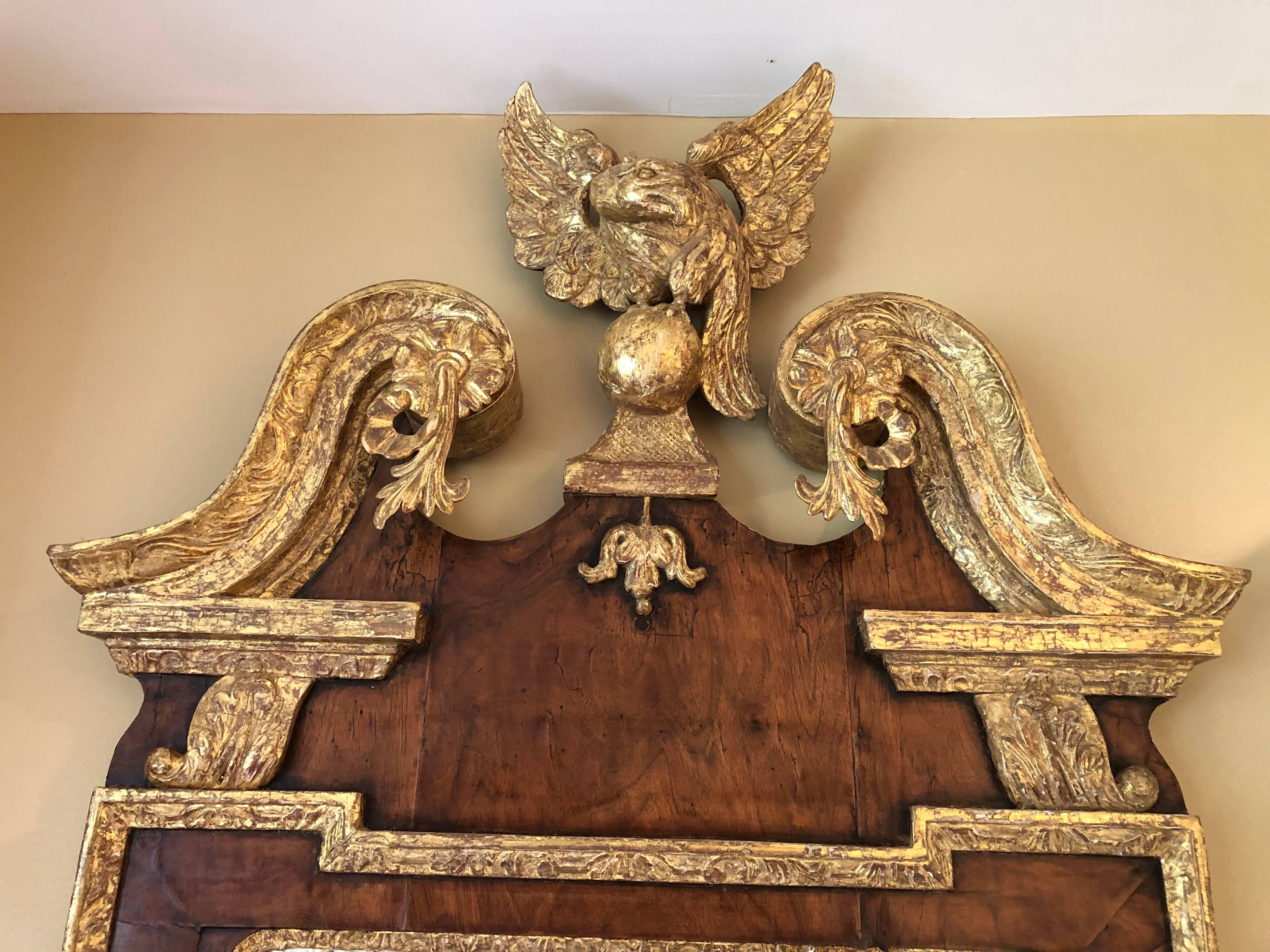 A George II walnut and parcel-gilt wall mirror, circa 1740. Upright beveled mirror plate within gilt leaf-tip carved moldings and a conforming veneered tigered walnut frame, the outer gilt gesso border carved with strap-work and flower heads, the