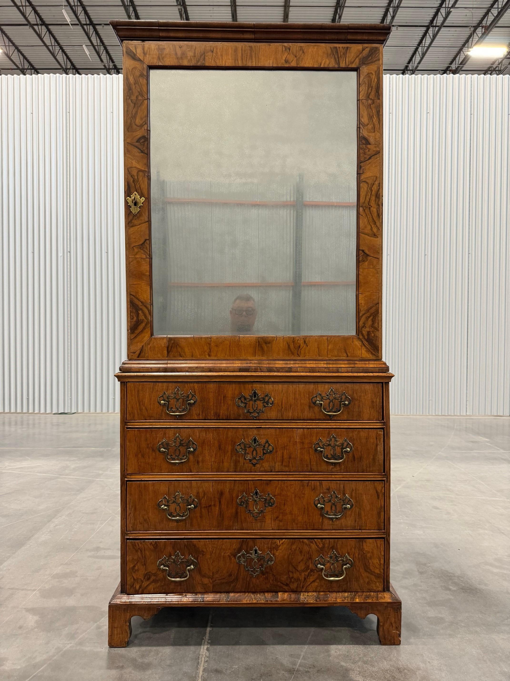A very nice and rare George II walnut cabinet on chest, the top section with mirror paneled door, and banded border concealing three adjustable shelves, the lower section fitted with four graduating drawers, each with book-matched veneer fronts,