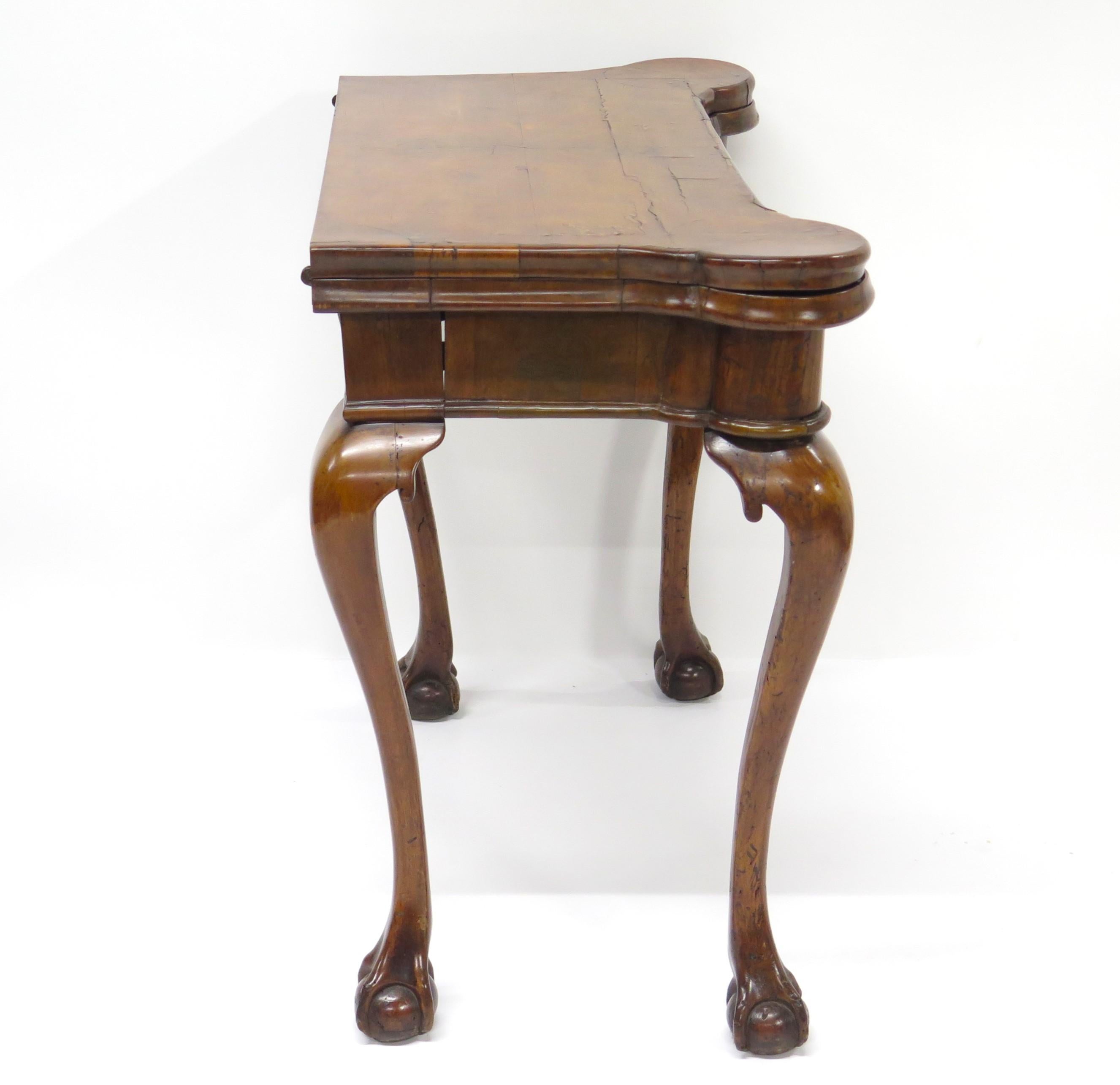 George II carved walnut card/games table that doubles as a side table when not in use. The fold over outset shaped top opens to reveal a baize lined playing surface with candle stands and guinea wells . Elegantly curved legs ending in a ball and