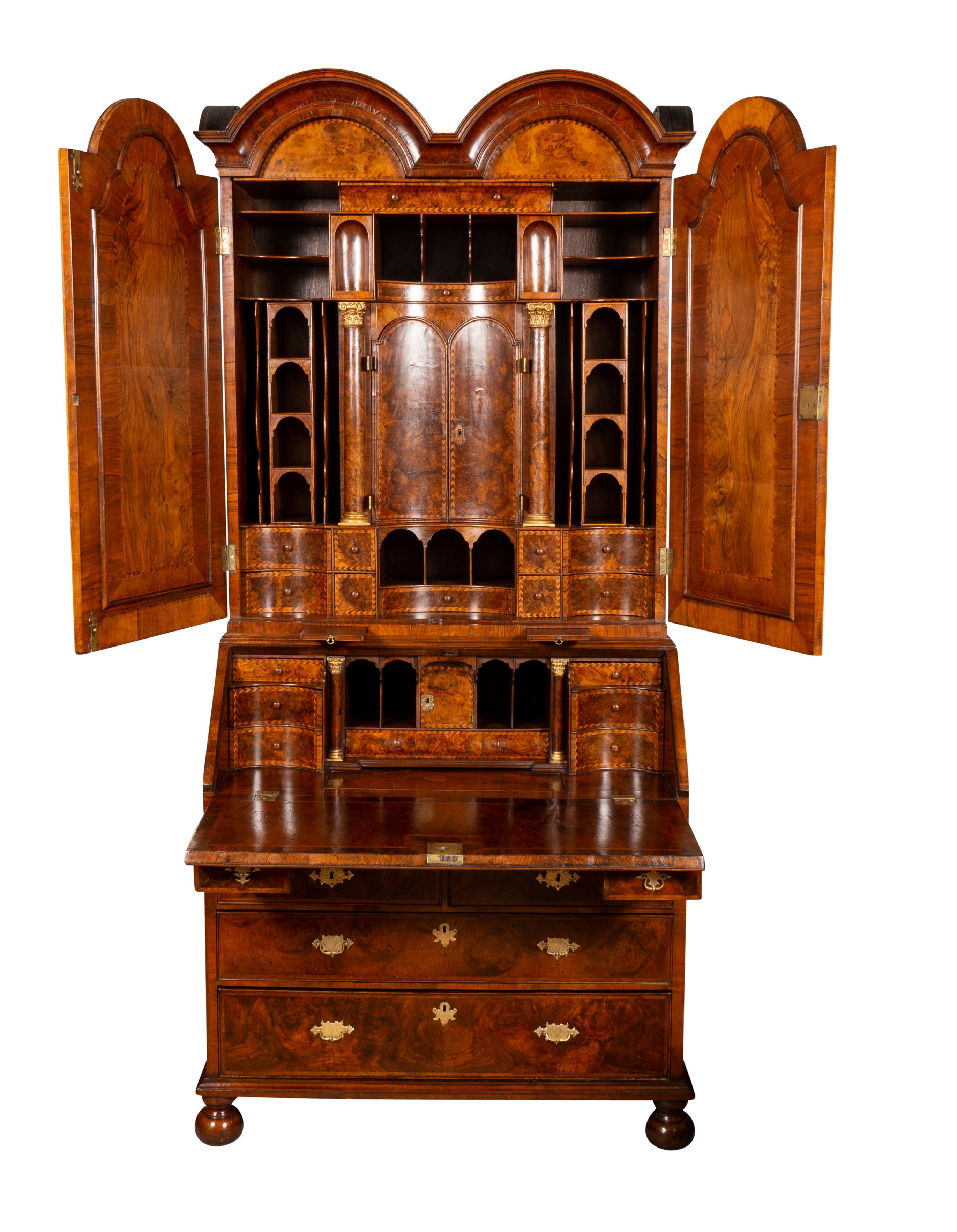 With double arch top over a pair of mirror doors opening to an elaborately fitted interior, the base with two candle slides and hinged slant lid writing surface opening to a fitted interior over two small candle drawers over two small drawers over