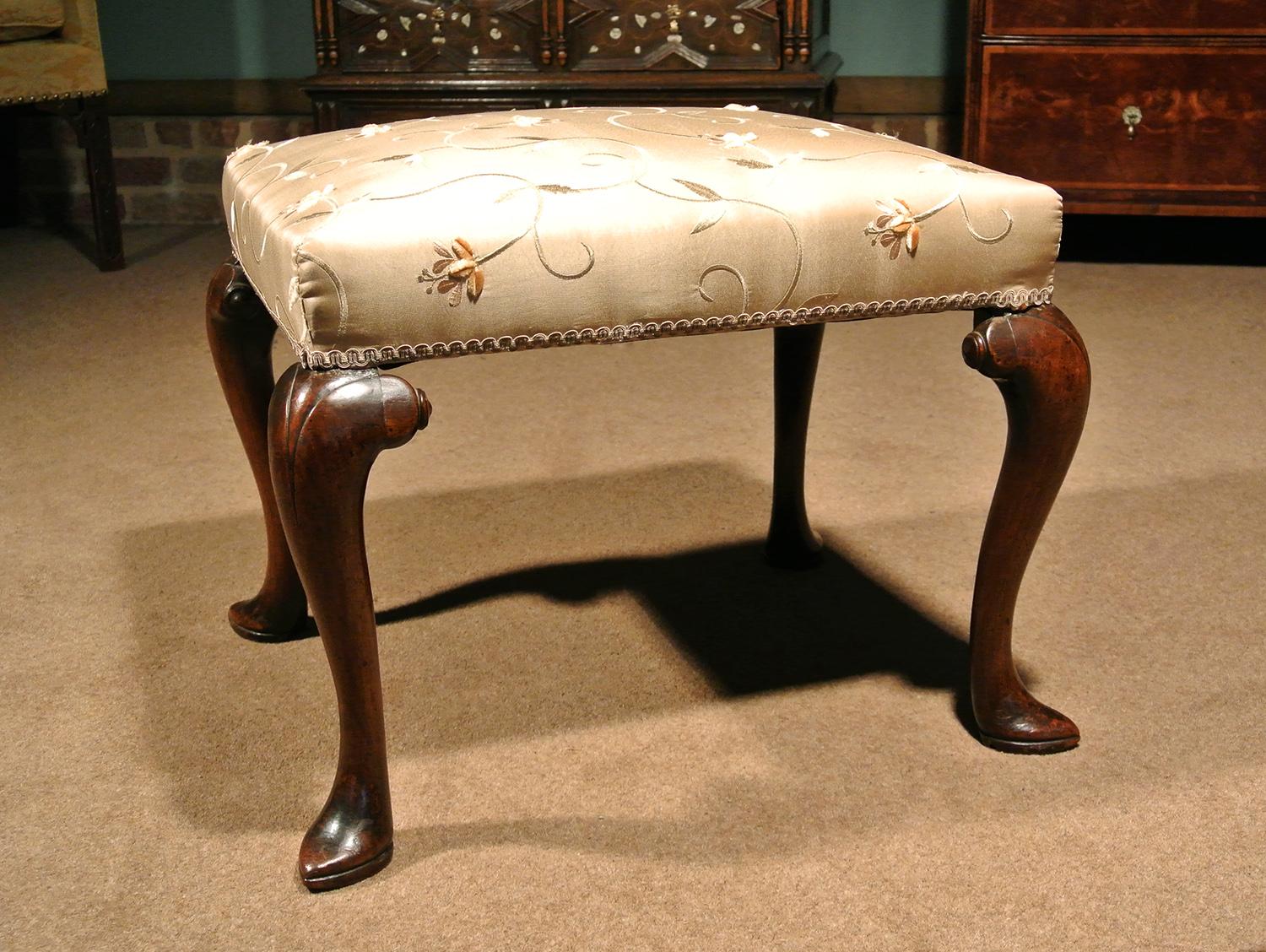 A beautiful walnut stool, circa 1740 with elegant slipper feet and broad scrolled hips terminating in small roundels.

A good colour and condition and retaining original pine seat rails. Newly re-upholstered in a top quality pure silk heavyweight