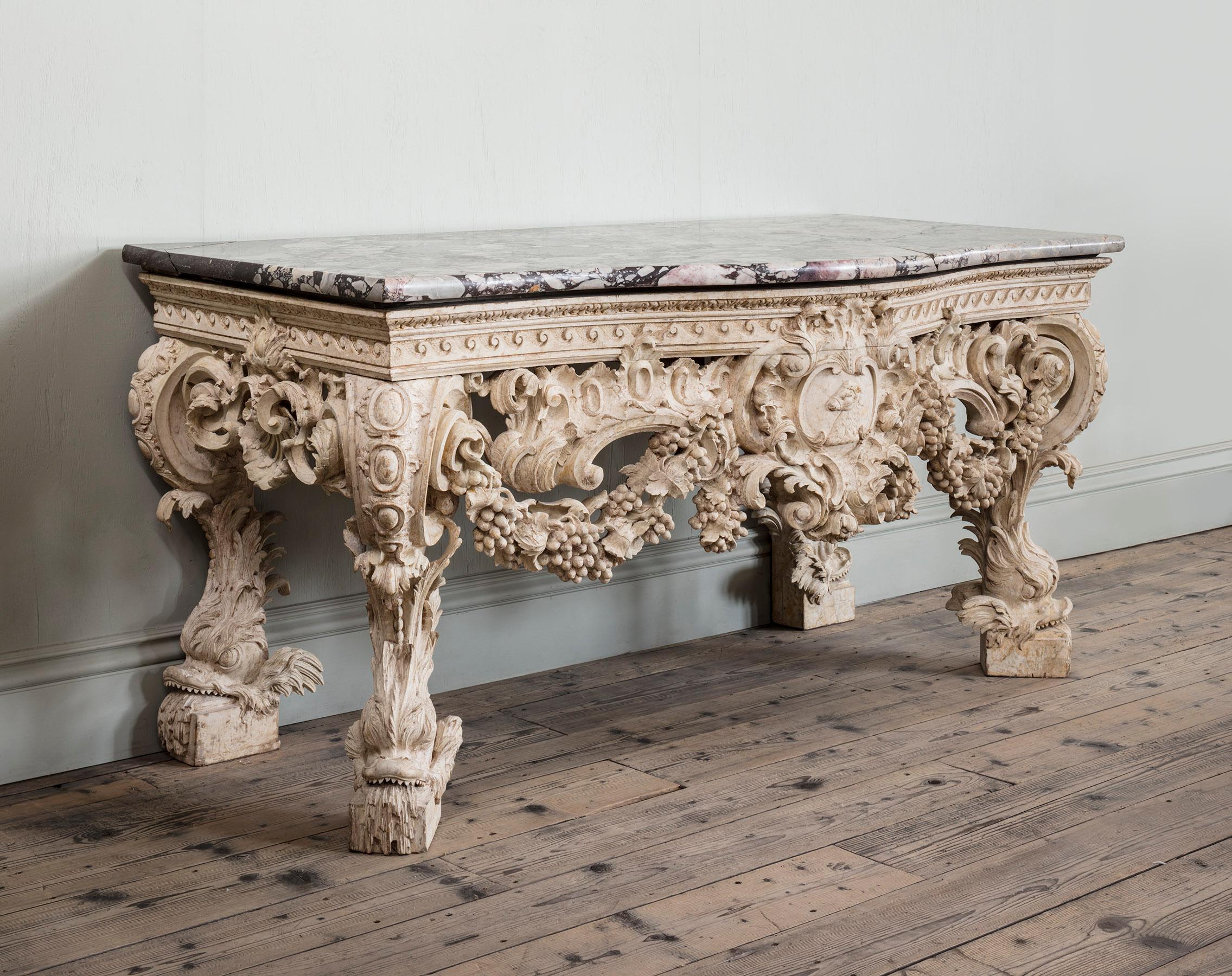 A George II White Painted Console Table
The original breche violette top, of serpentine form, sits above a handsomely carved Vitruvian scroll frieze, backed by pounced detailing. The table is centred by a scrolling and foliate cartouche,
