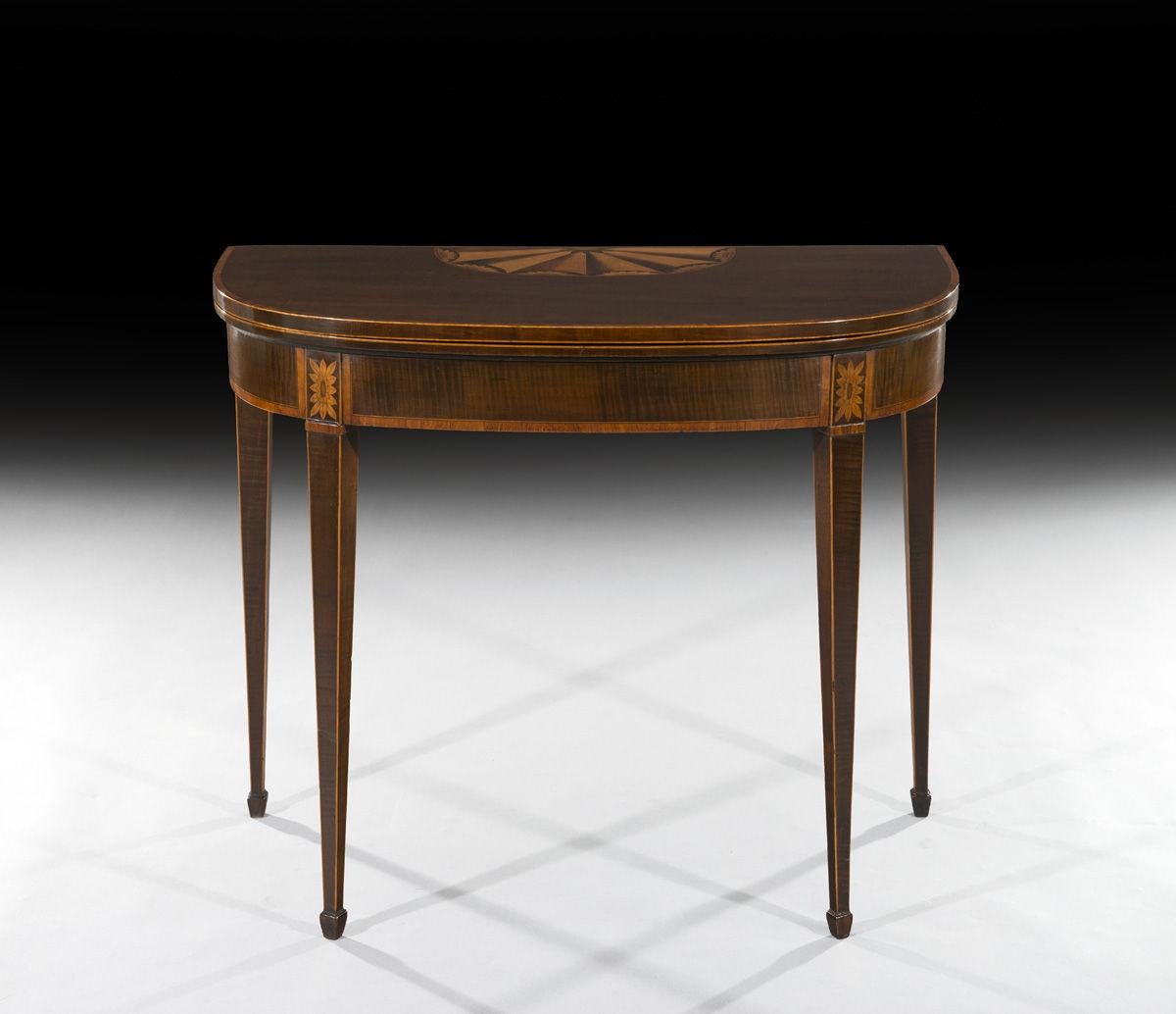 The D-shaped top is veneered in harewood, inlaid with a large fanned medallion and cross-banded in kingwood and the top opens to reveal a green baize playing surface which sits on a scissor-action gate leg support. The satinwood cross banded frieze