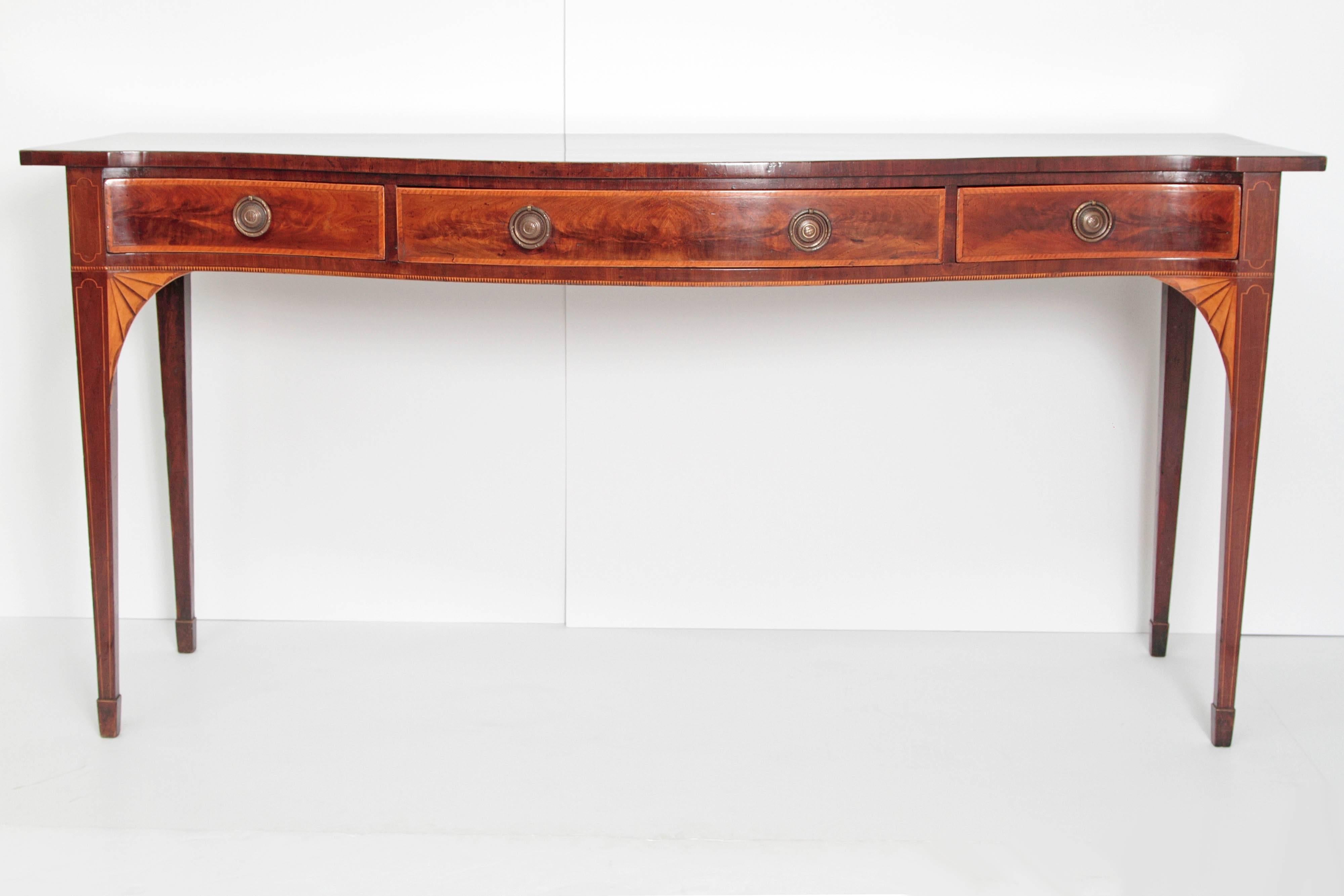 A fine English George III mahogany sideboard with satin wood inlays. An exquisitely figured single serpentine plank bow front top with satin wood stringing. The serpentine front consists of two small concave drawers left and right with a convex