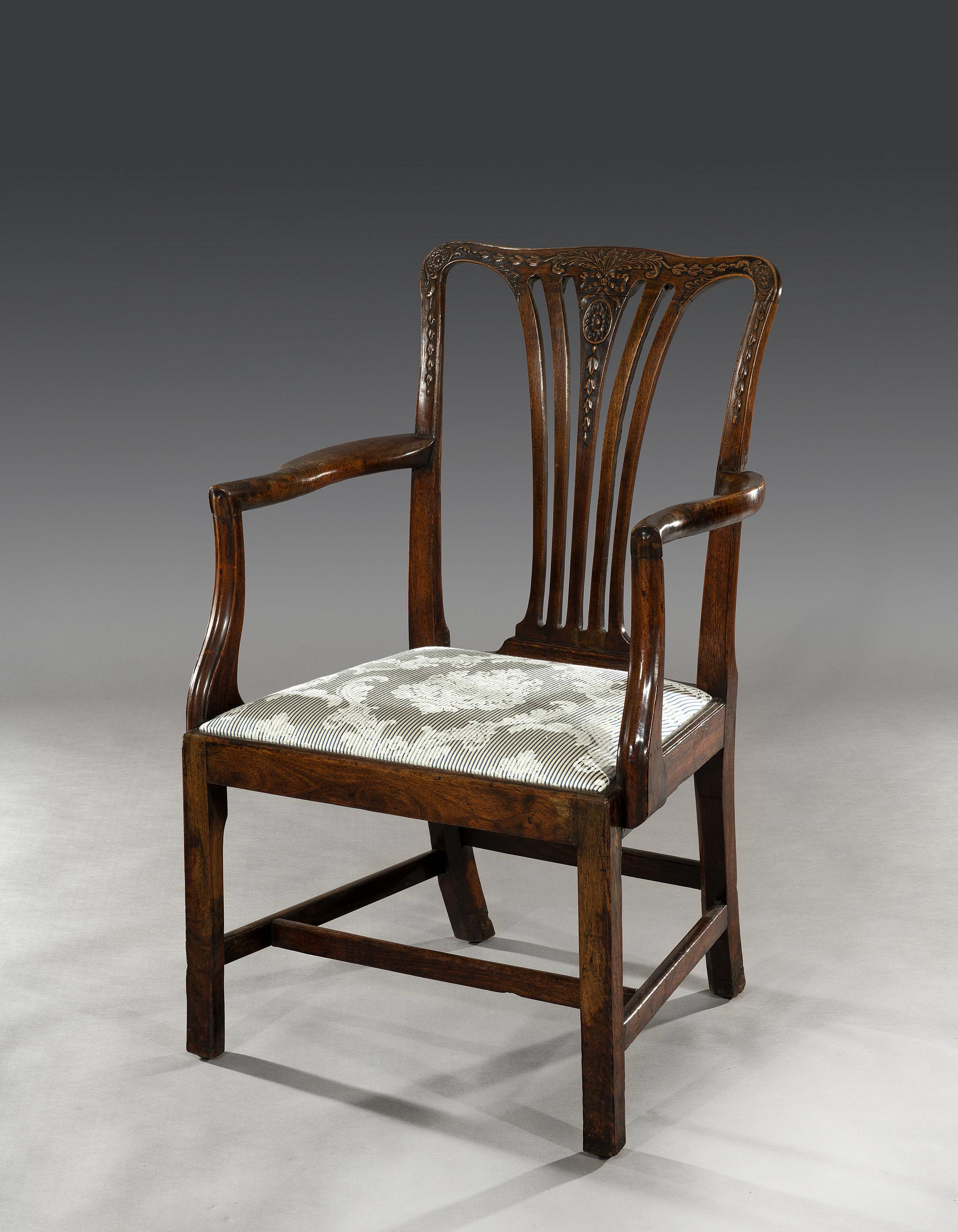 The walnut chair is decorated with ribbons, flowerbells and patere carvings reminiscent of Robert Adam designs. The drop-in seat has been recently re-upholstered in a blue and white damask fabric. Above you have solid burr walnut arms that support