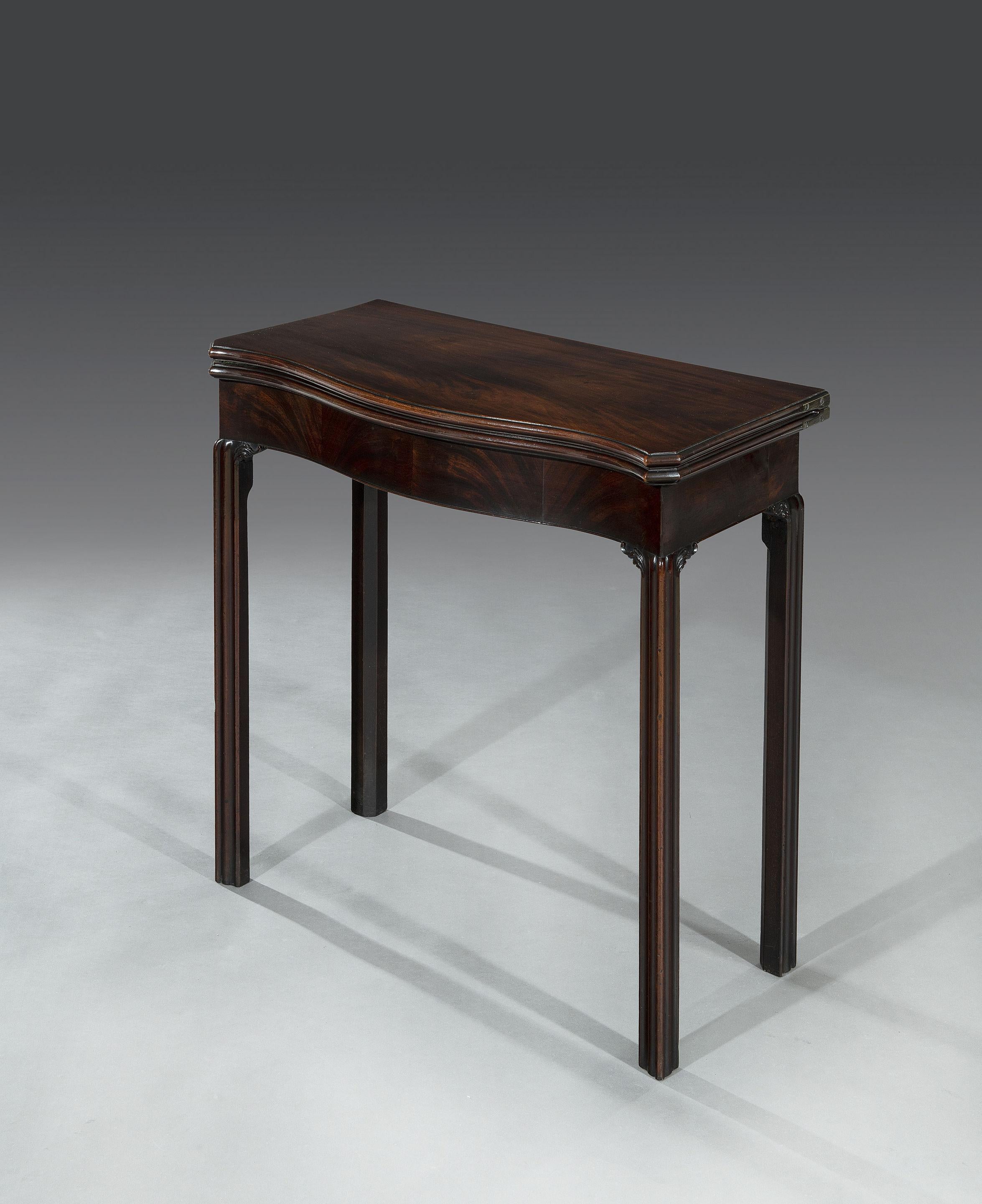 The serpentine veneered top opens to reveal a green baize playing surface and is supported by a single gate leg action to the rear. When the gate leg is used it reveals a concealed single oak lined drawer. The rounded moulded edge sits above the