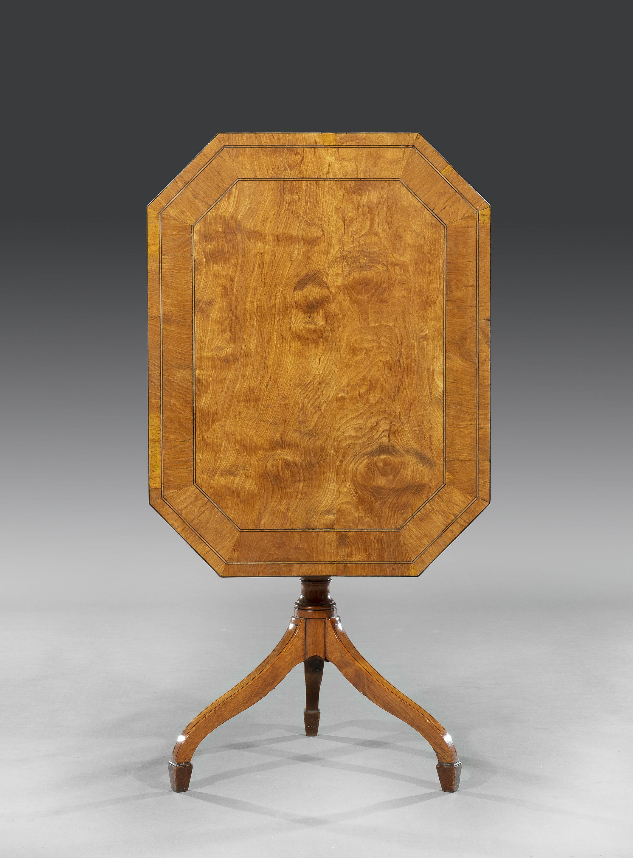 The octagonal shape tilt-top table with West Indian satinwood veneers is cross-banded in satinwood with ebony stringing and satinwood banding and sits on a solid satinwood turned pedestal base on splayed ebony strung legs that terminate on block