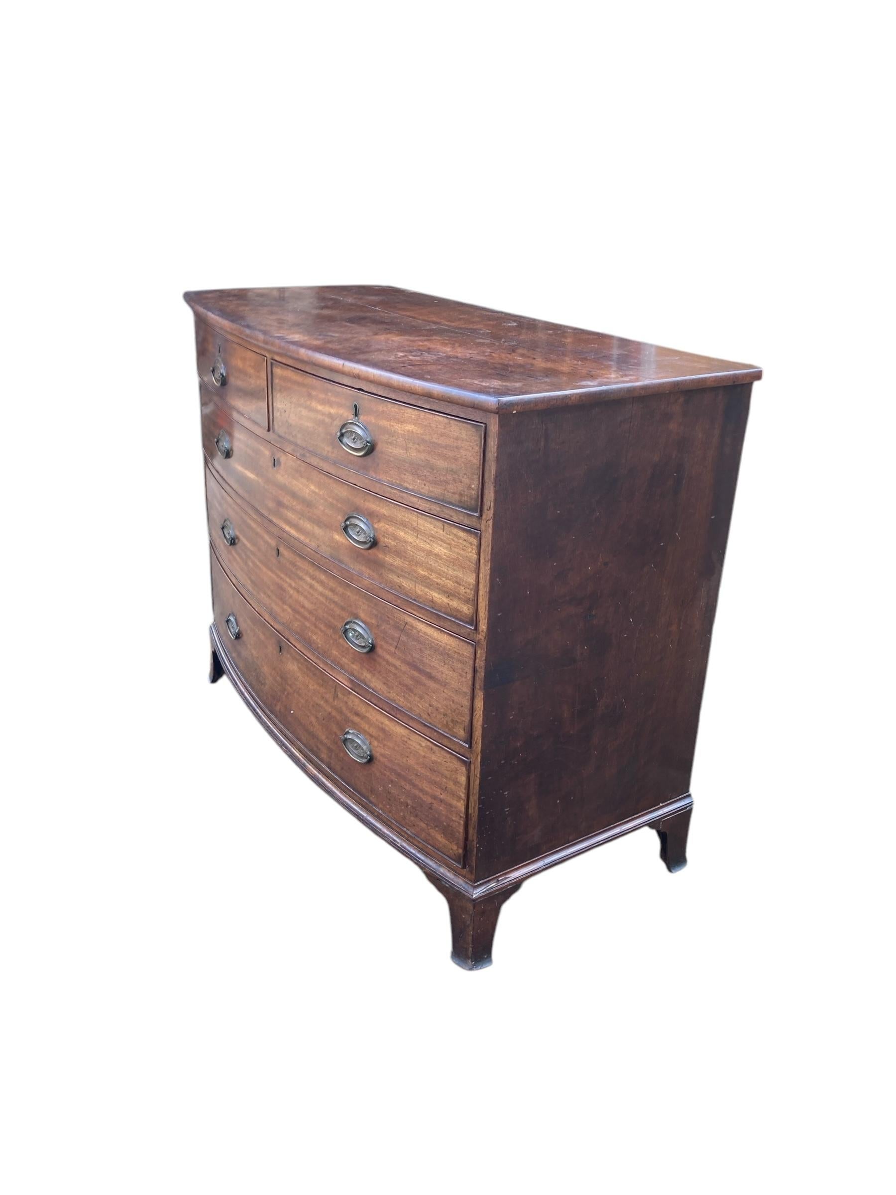 George III 19th Century mahogany bowfront chest of drawers, having a nice figured top above a selection of two short over three long oak lined graduated drawers, with oval brass plate handles. Circa 1800. Minor losses to handles but does not effect