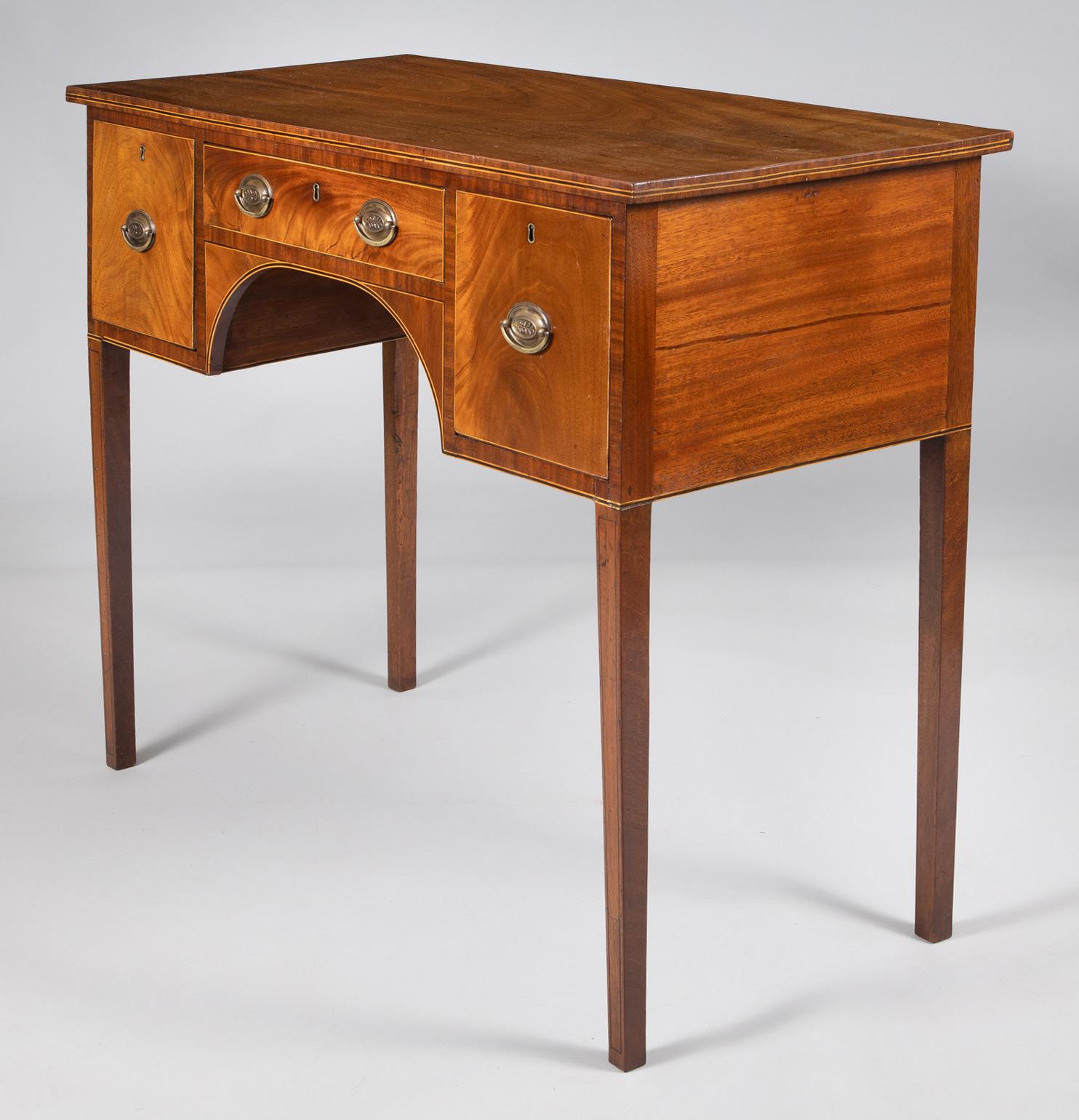 George III mahogany small sideboard with boxwood and ebony stringing around the top edge, above a central frieze drawer and kneehole flanked by two deep drawers, all outlined with boxwood and ebony stringing, the drawers with brass oval handles and