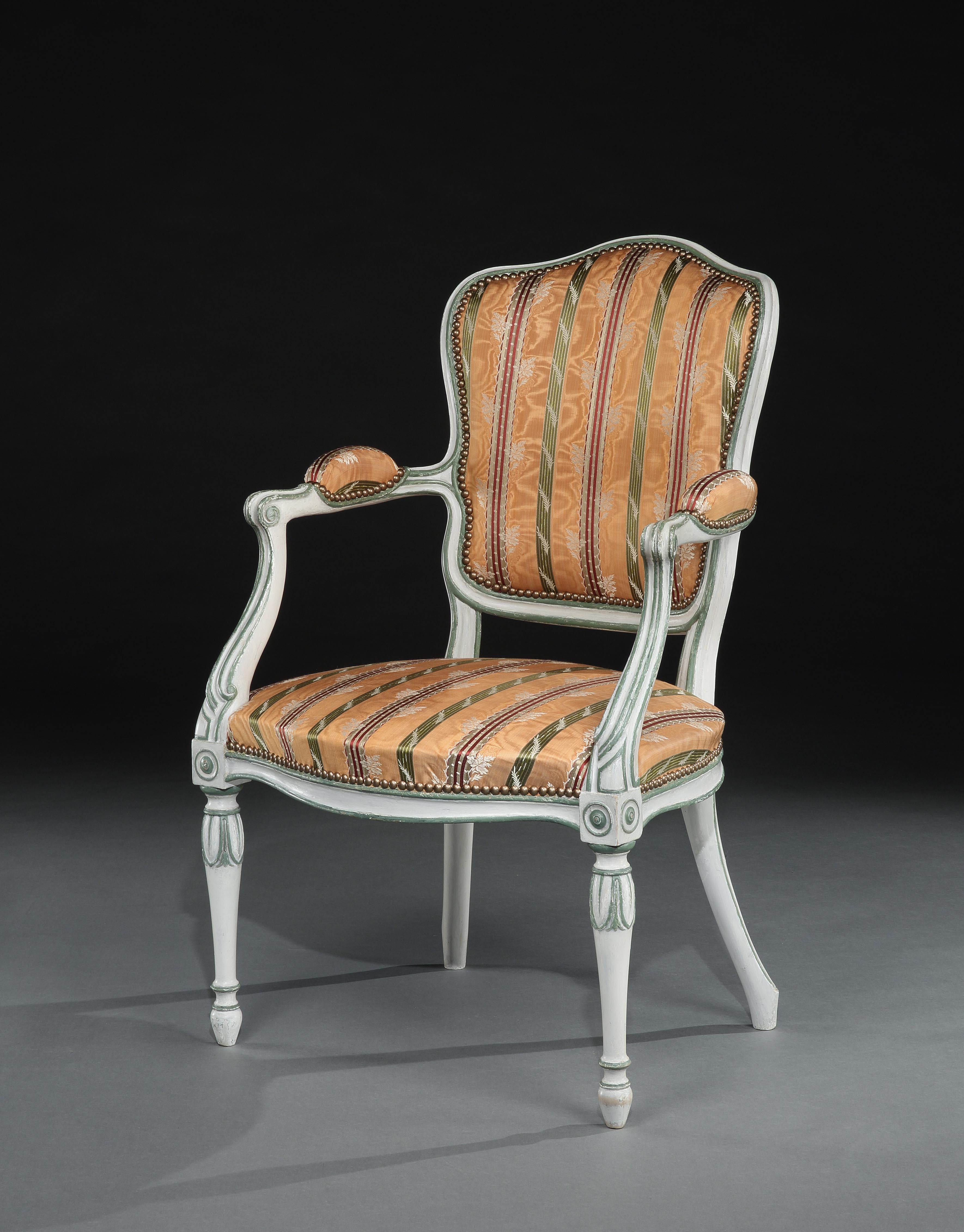 A fine George III painted open armchair in the French Hepplewhite taste. The shield shaped back, serpentine seat and arm-rests upholstered. The chair frame with channeled detailing painted off-white with green highlights. The shield shaped back with
