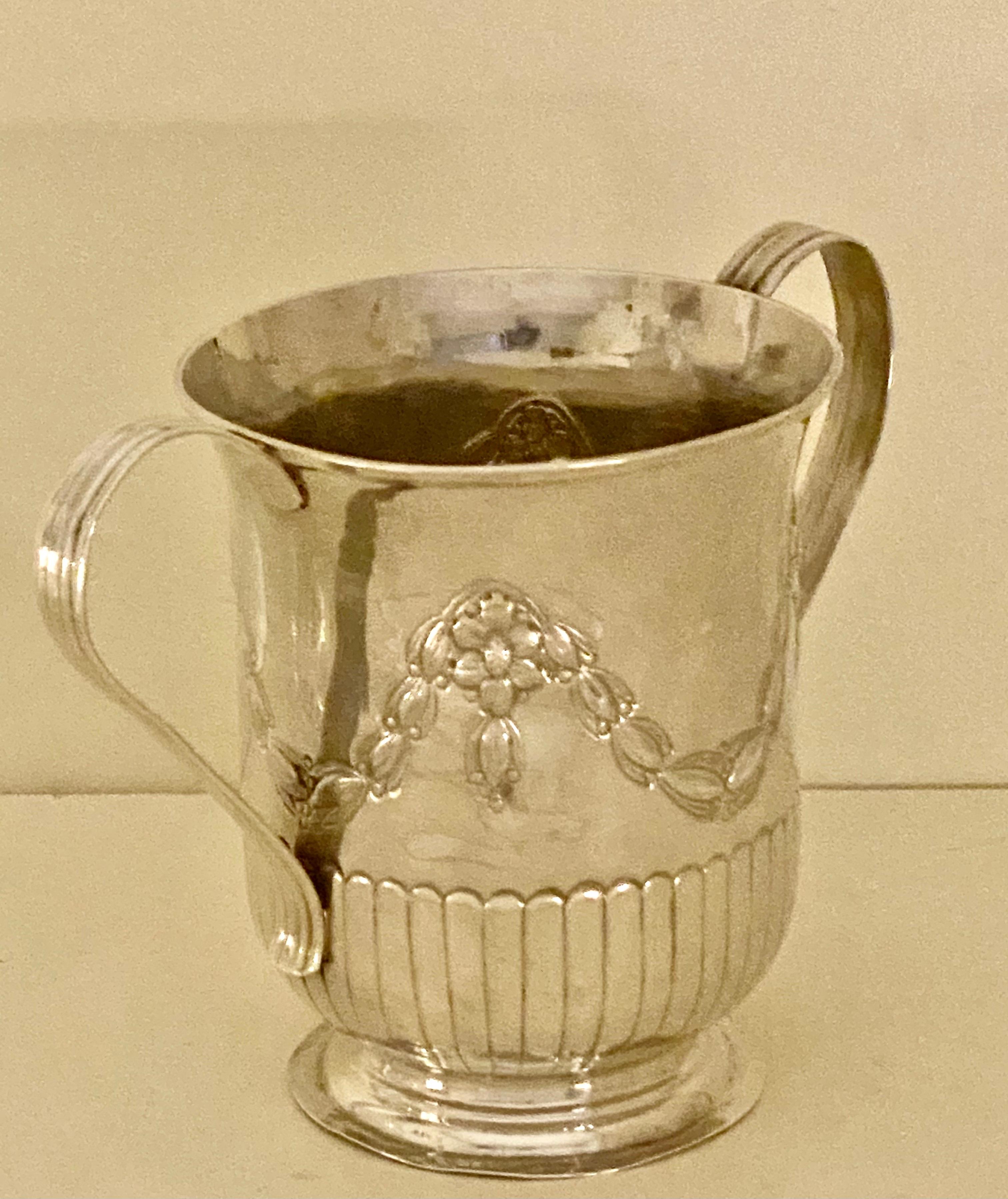 An antique sterling silver 2 handled porringer from the reign of George III with pretty decoration and a flat base. Embossed decoration with flowers and leaves to the upper body and a ribbed border all the way round the lower body. To the front